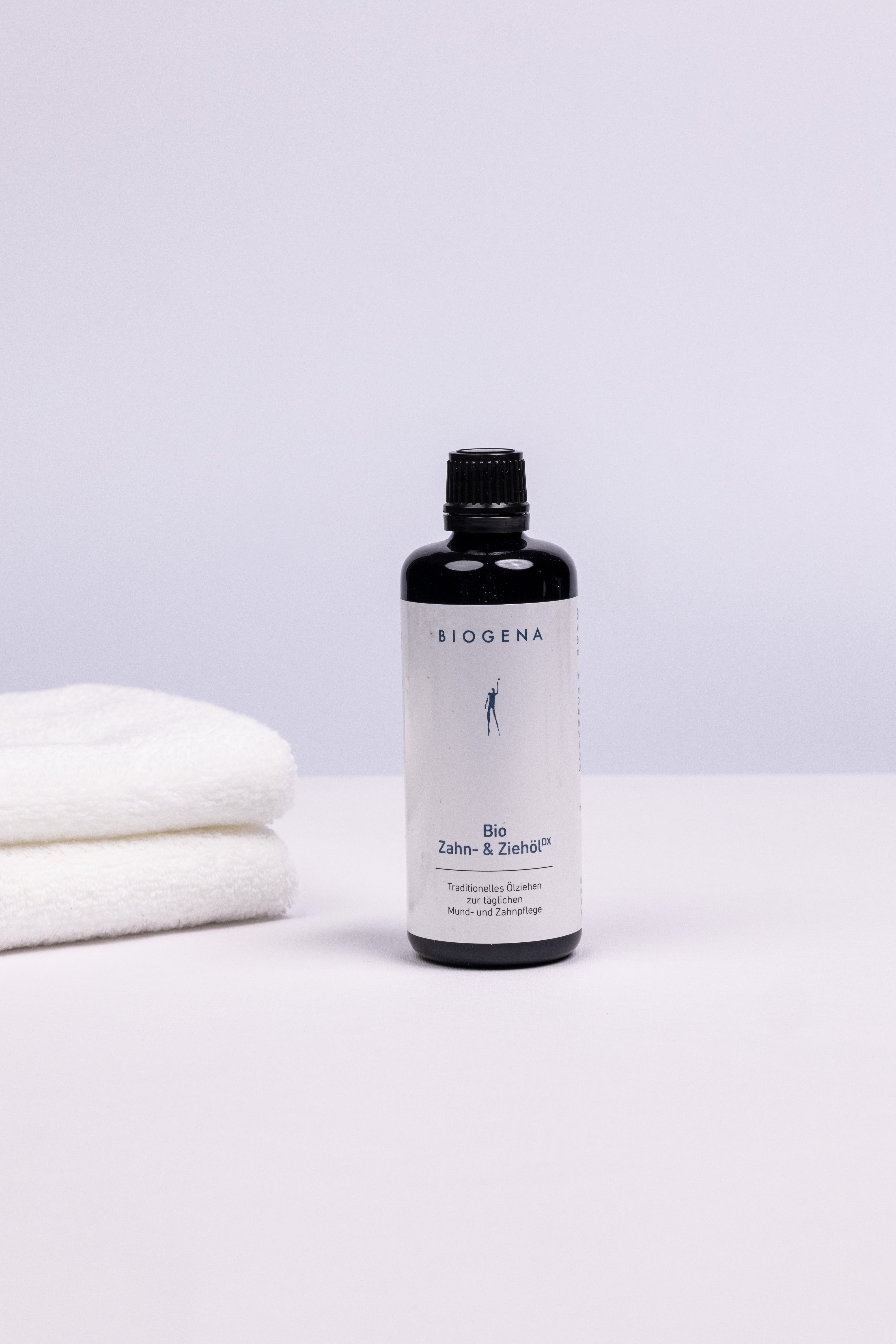 BIOGENA Zahn- und Ziehöl Flasche stehend, links daneben ein Stapel weißer Handtücher.