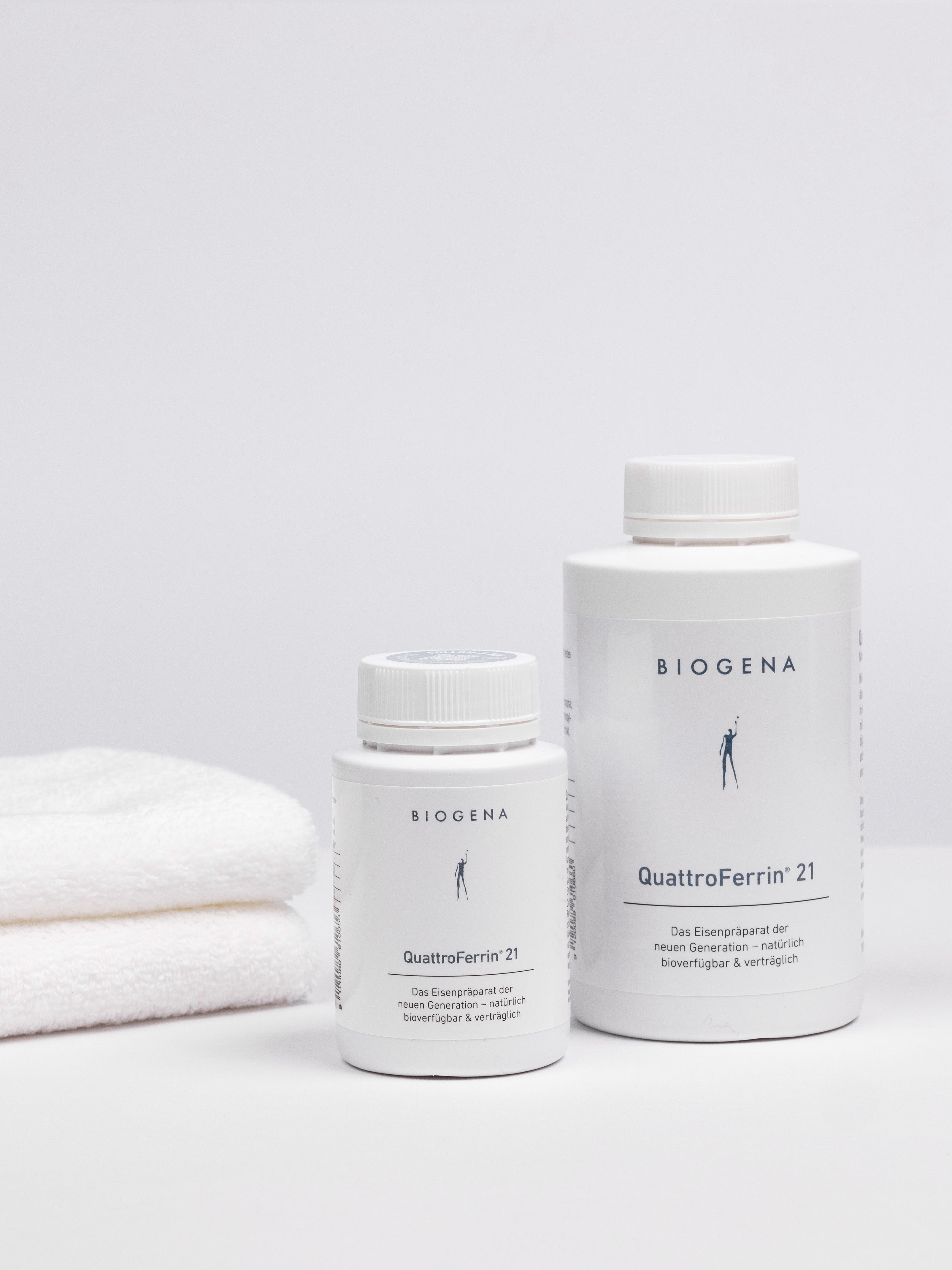 Zwei Dosen QuattroFerrin 21 unterschiedlicher Verpackungsgrößen stehend, links daneben ein Stapel weißer Handtücher.