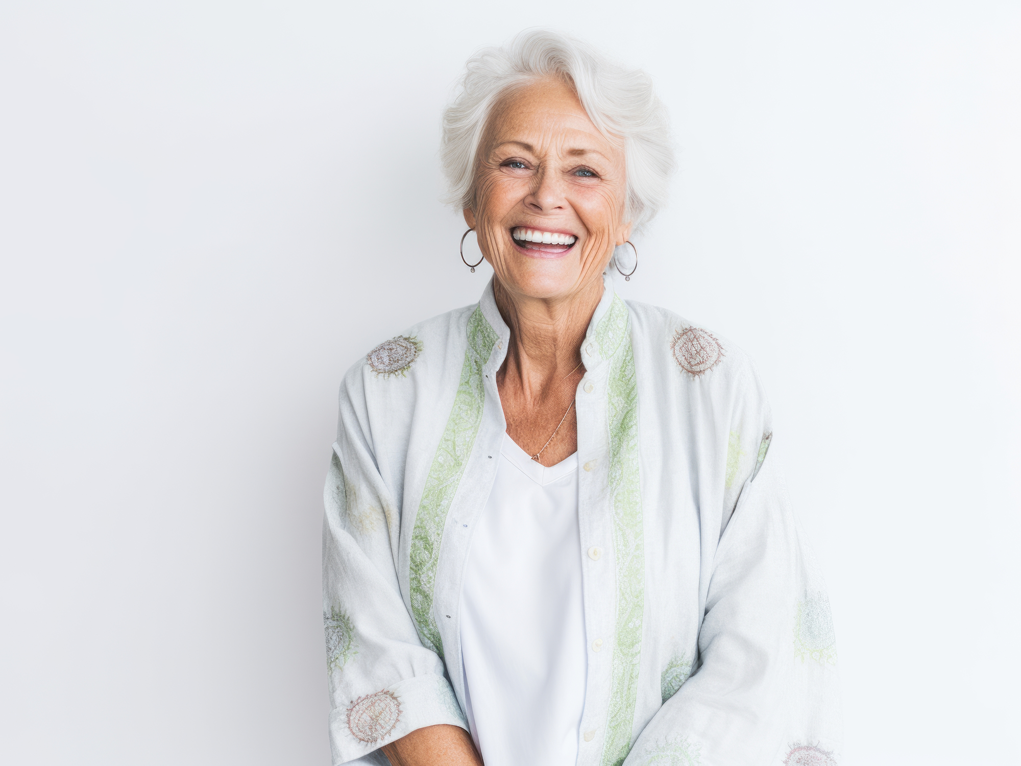 Ältere Frau mit weißen Haaren und großen Ohrringen und heller Kleidung lacht herzlich.