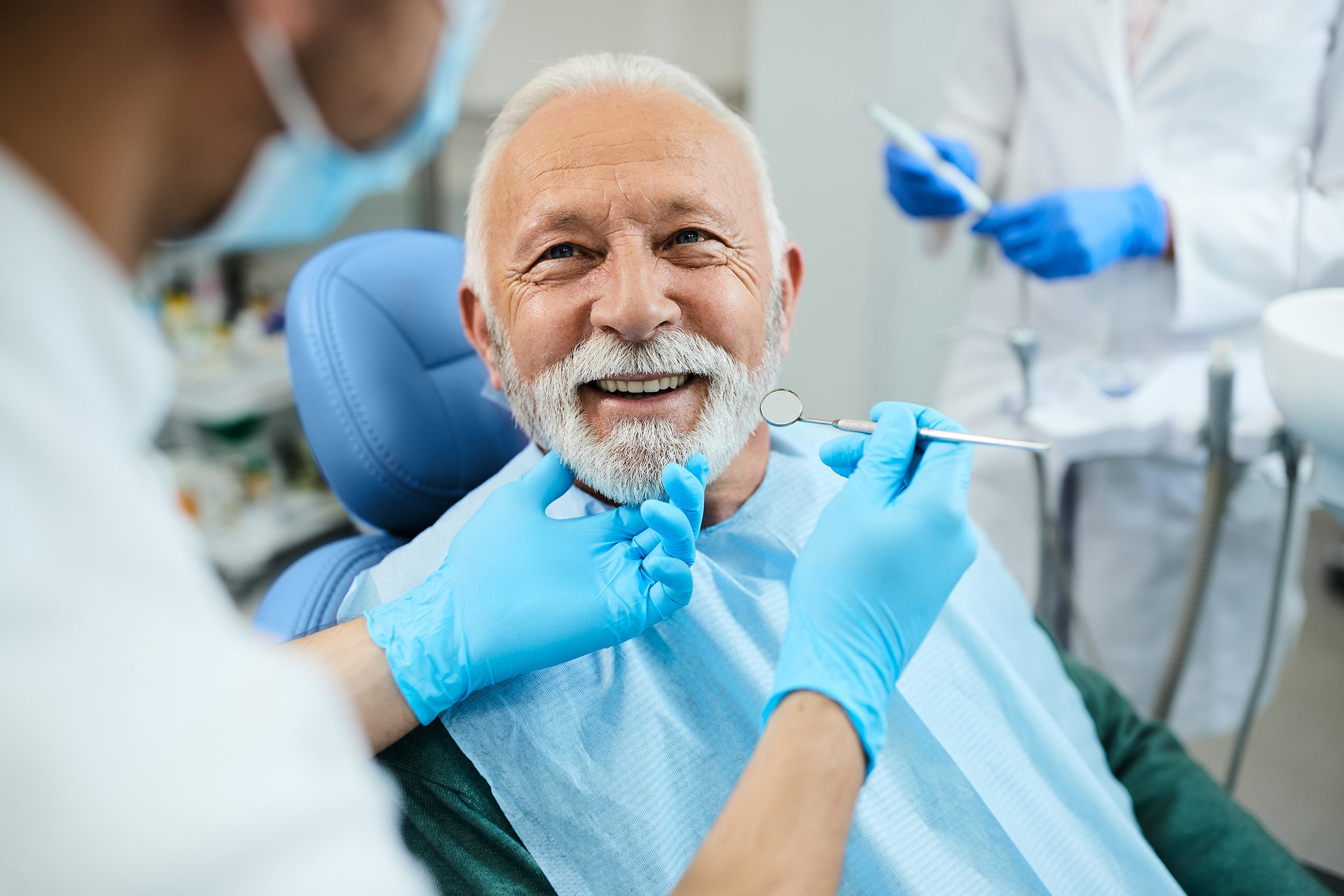 Älterer Patient sitzt auf dem Behandlungsstuhl einer Zahnarztpraxis und lächelt seinen behandelnden Zahnarzt an.