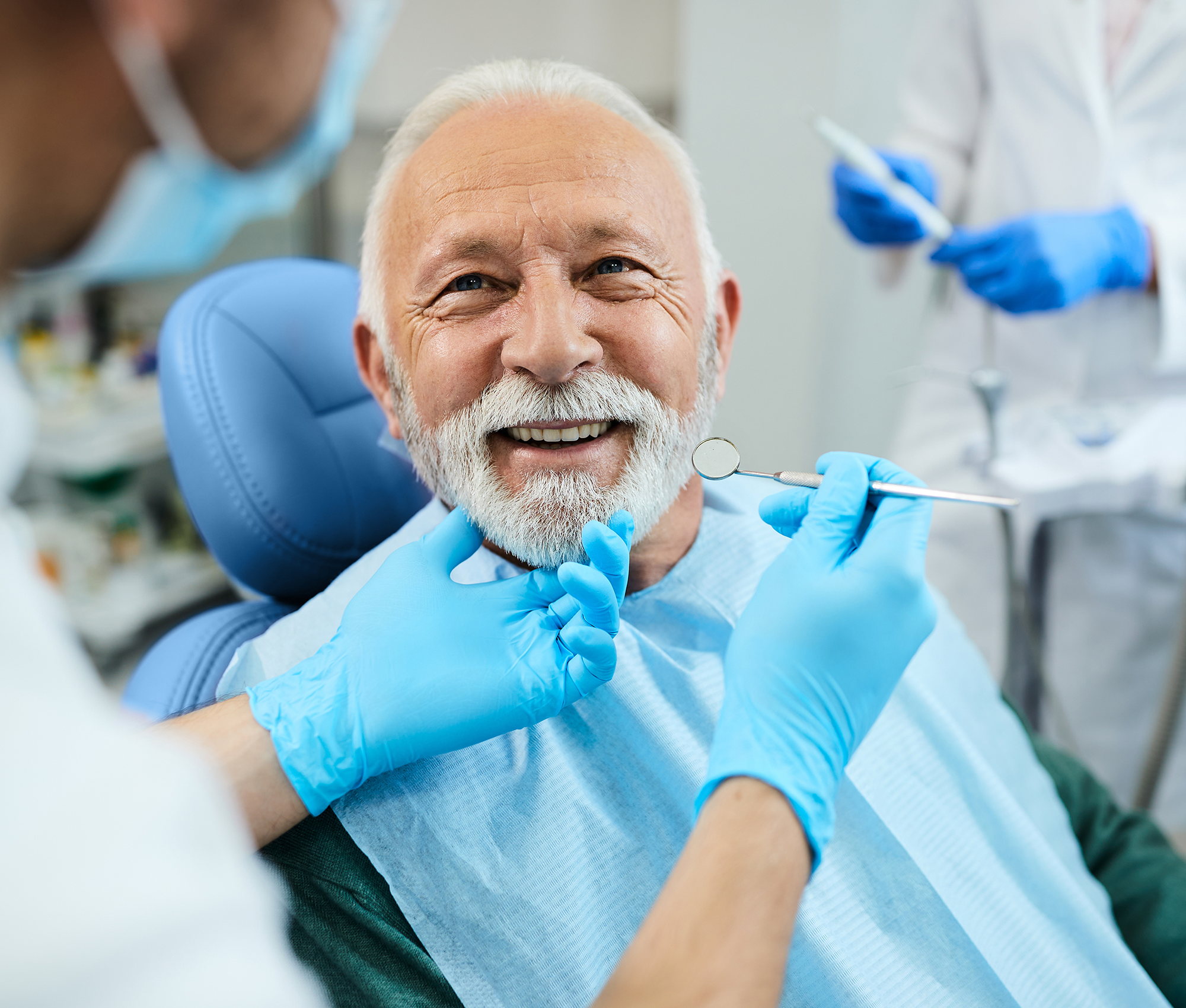 Älterer Patient sitzt auf dem Behandlungsstuhl einer Zahnarztpraxis und lächelt seinen behandelnden Zahnarzt an.