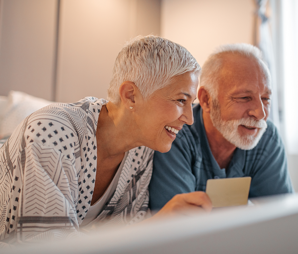 Älteres Pärchen blicken zusammen Laptop und lächeln herzlich.