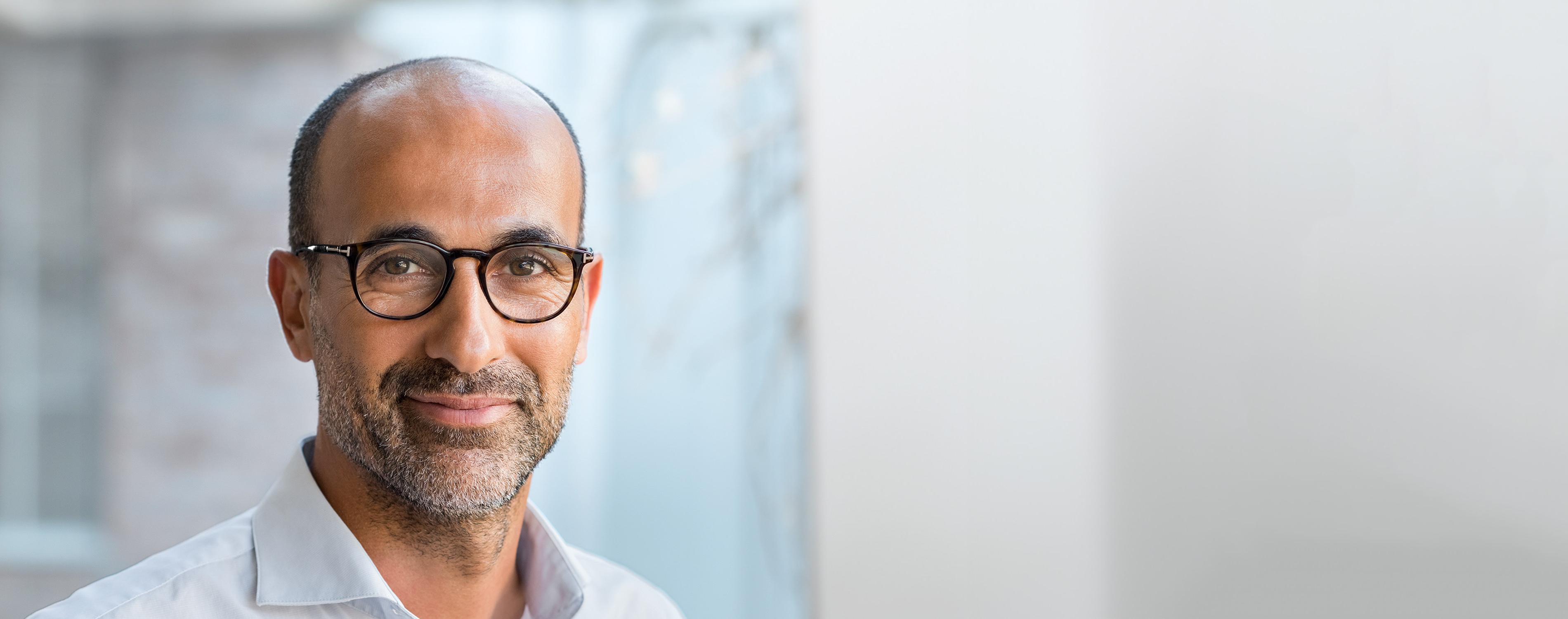 Mann mittleren Alters mit schwarzen kurzen Haaren, braunen Augen und einer dunklen Brille schaut lächelnd frontal in die Kamera.