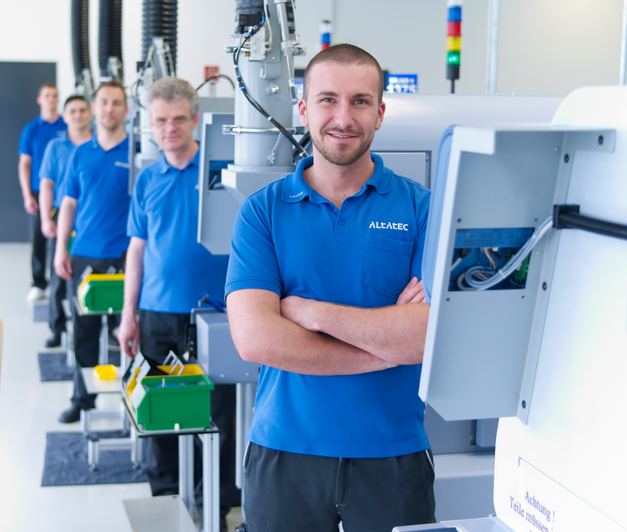 Mitarbeiter der Altatec GmbH, Exklusivhersteller der Camlog Implantate, stehen hintereinander neben Maschinen in der Produktionshalle.
