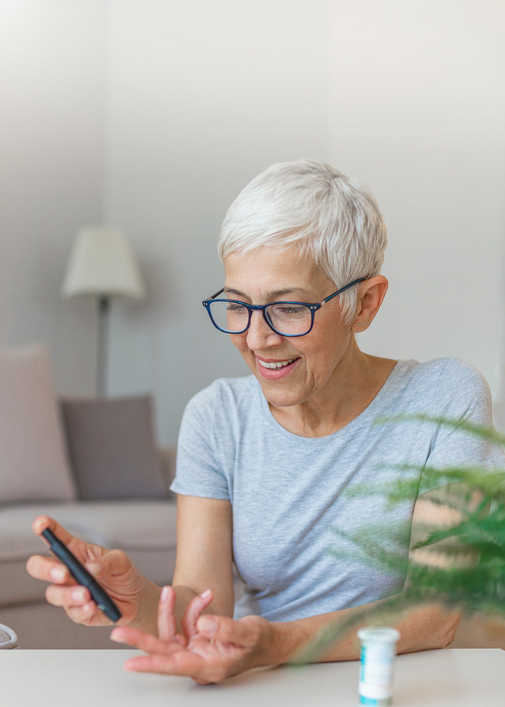 Ältere Frau mit kurzen weißen Haaren und einer Brille misst sich mit einem Diabetesmessgerät am linken Mittelfinger den Blutzucker.