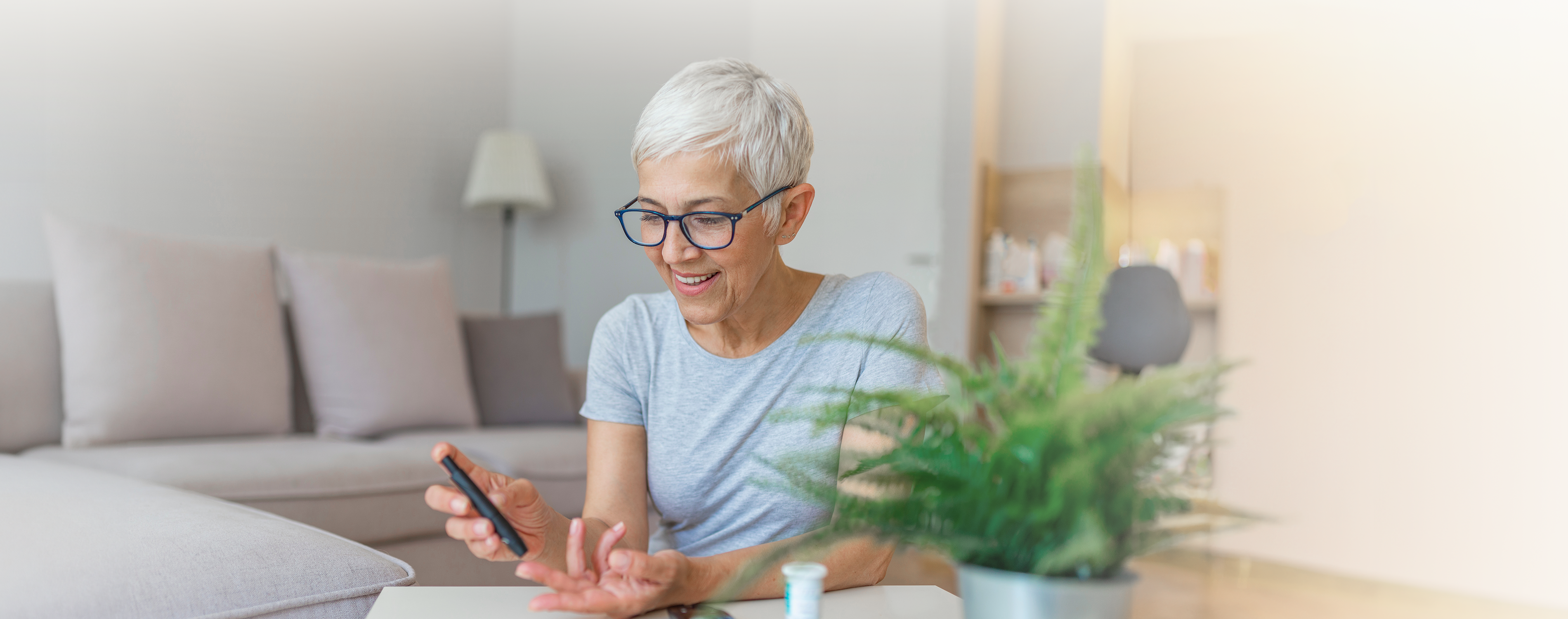 Ältere Frau mit kurzen weißen Haaren und einer Brille misst sich mit einem Diabetesmessgerät am linken Mittelfinger den Blutzucker.