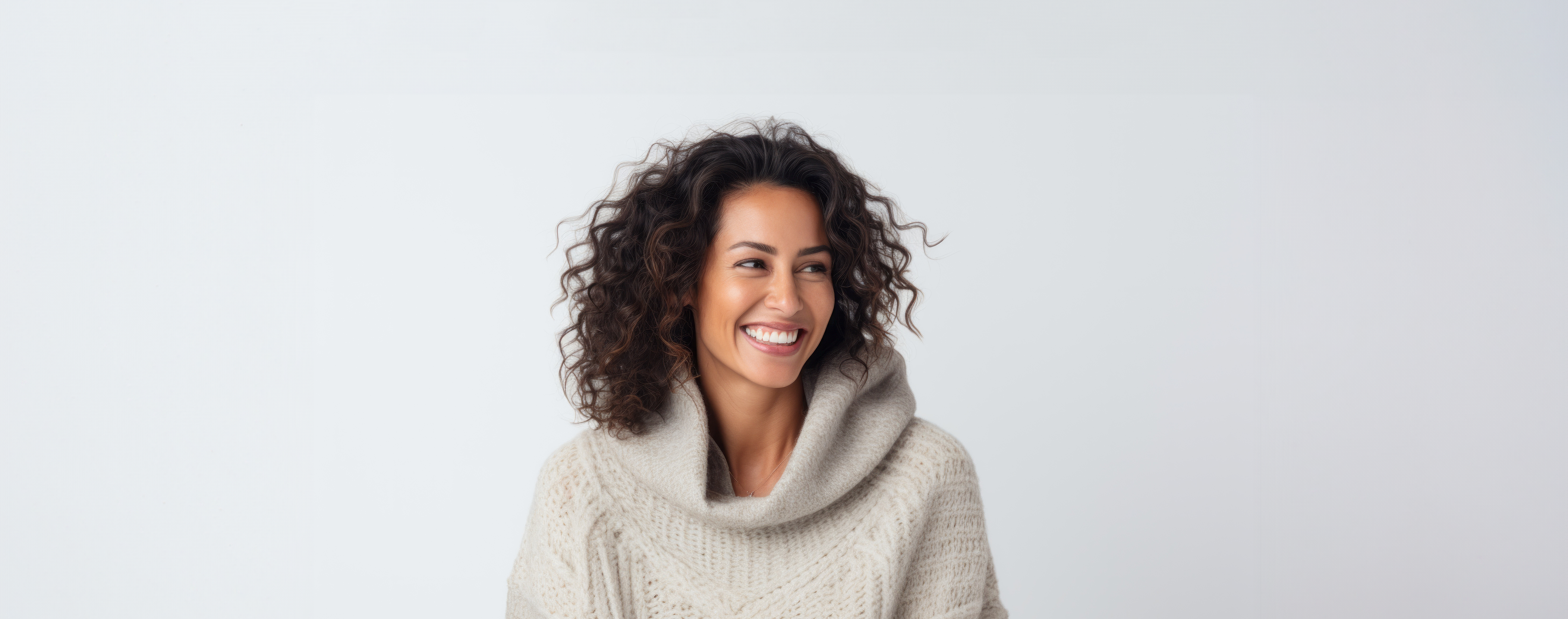 Junge Frau mit schulterlangen, lockigen, braunen Haaren trägt einen beigen Strickpullover. Sie lacht abgewandt zur rechten Seite.