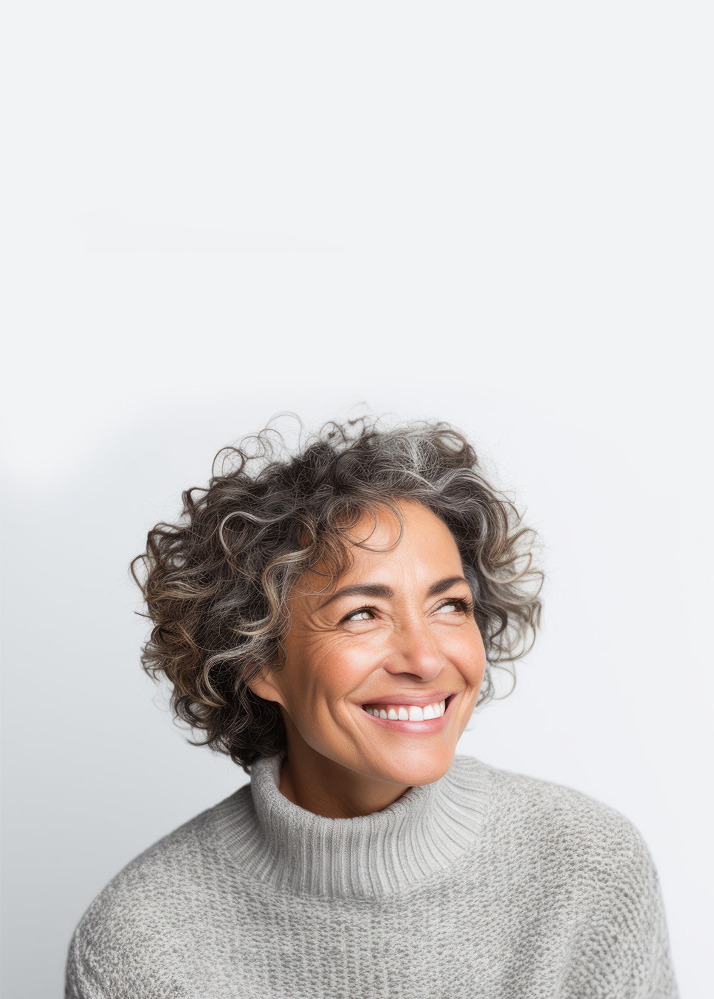 Frau mit schulterlangen, lockigen, braun-grauen Haaren trägt einen grauen Strickpullover. Sie lacht abgewandt zur rechten Seite.