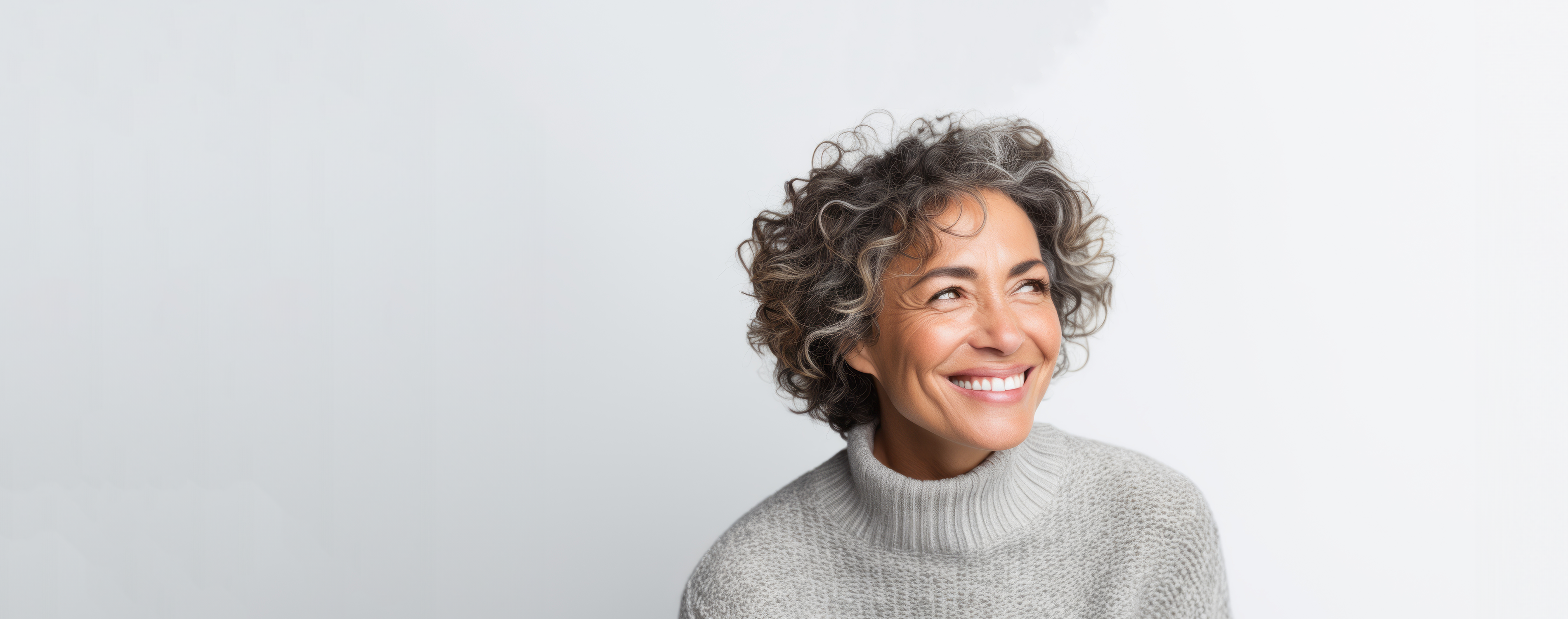 Frau mit schulterlangen, lockigen, braun-grauen Haaren trägt einen grauen Strickpullover. Sie lacht abgewandt zur rechten Seite.