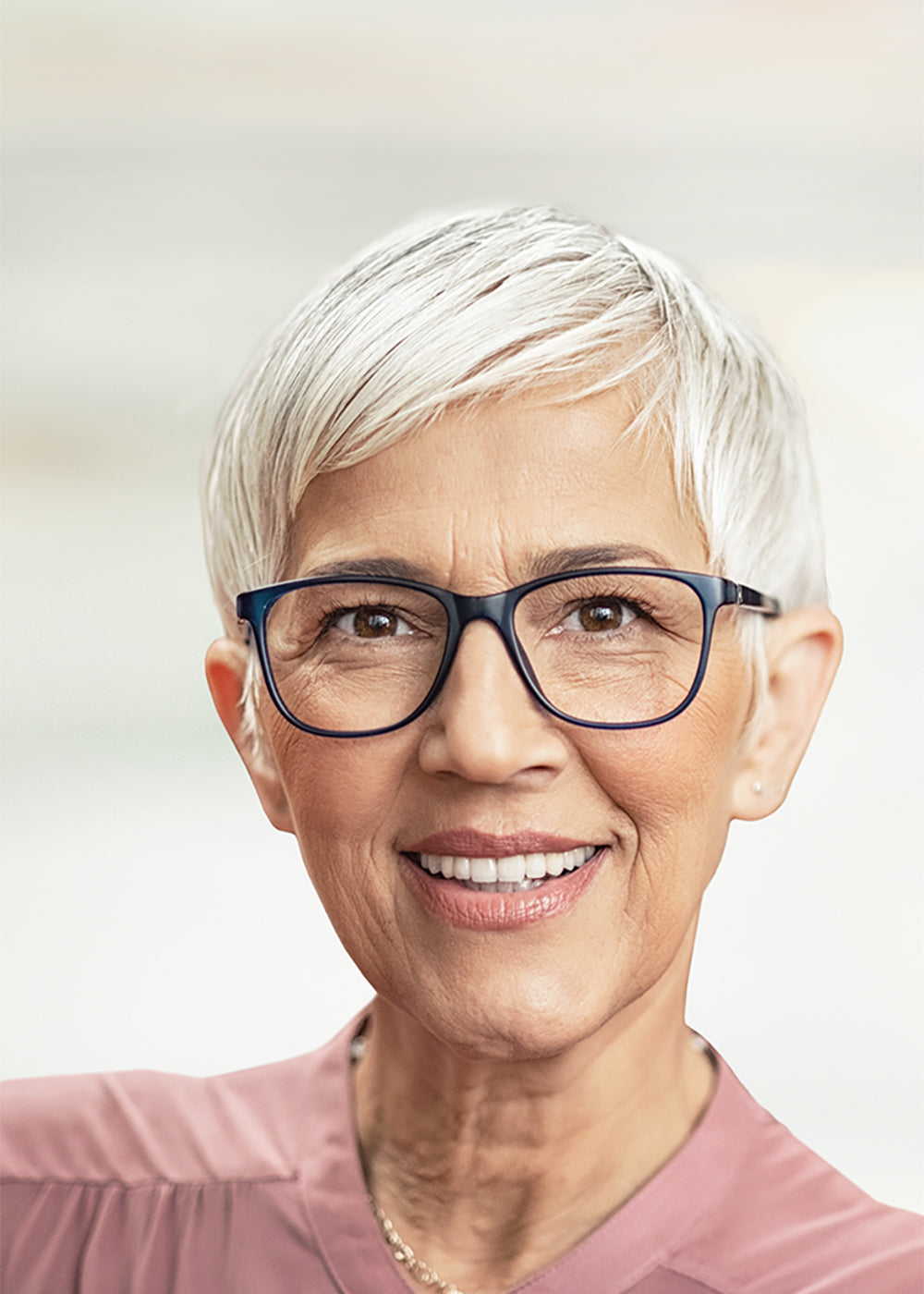 Junge lächelnde Frau isst Joghurt mit Beeren, mit einem Löffel in der rechten Hand und dem Joghurtglas in der linken Hand.