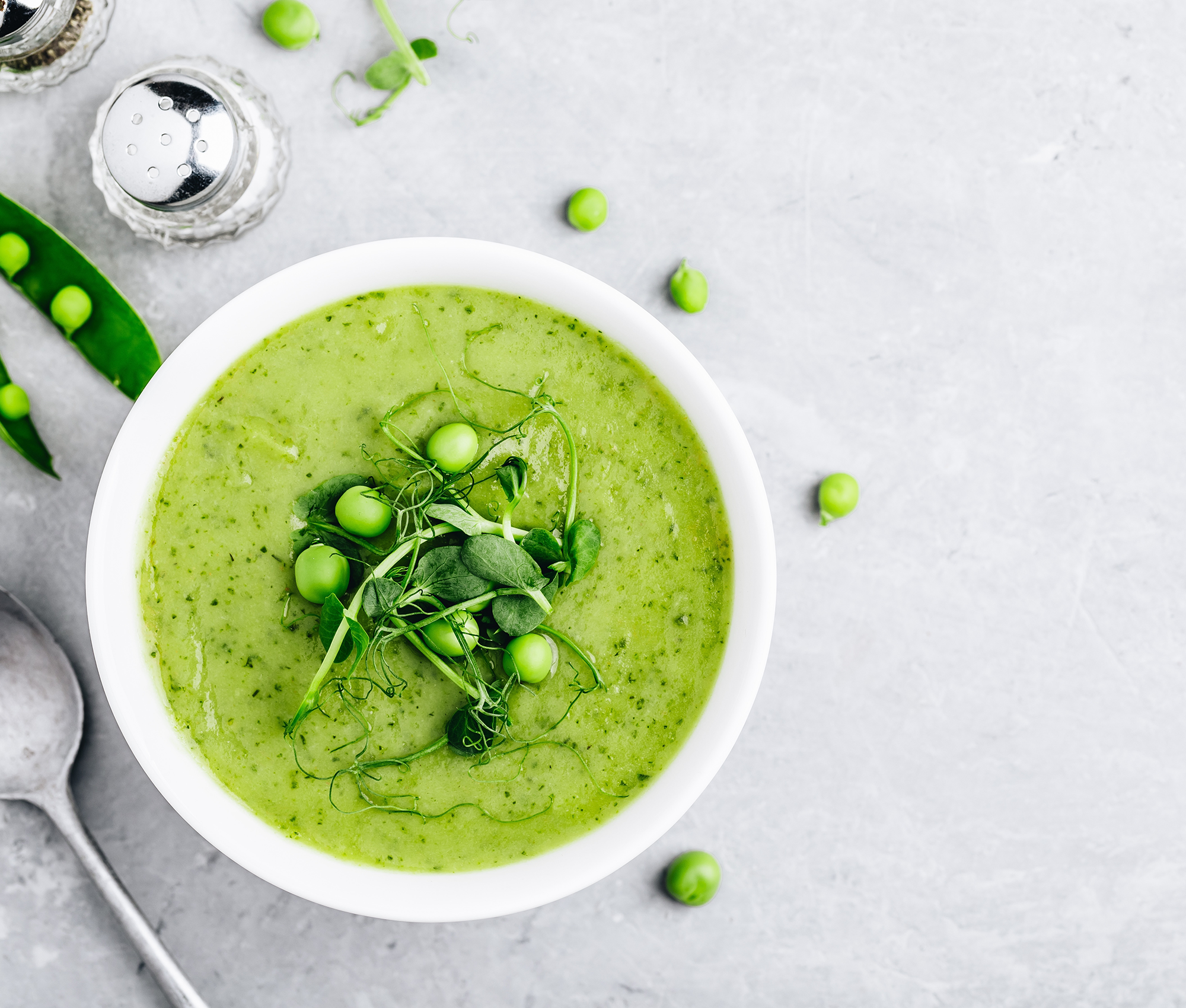 Grüne Suppe in einer weißen Suppenschale, links davon ist ein Esslöffel abgebildet.