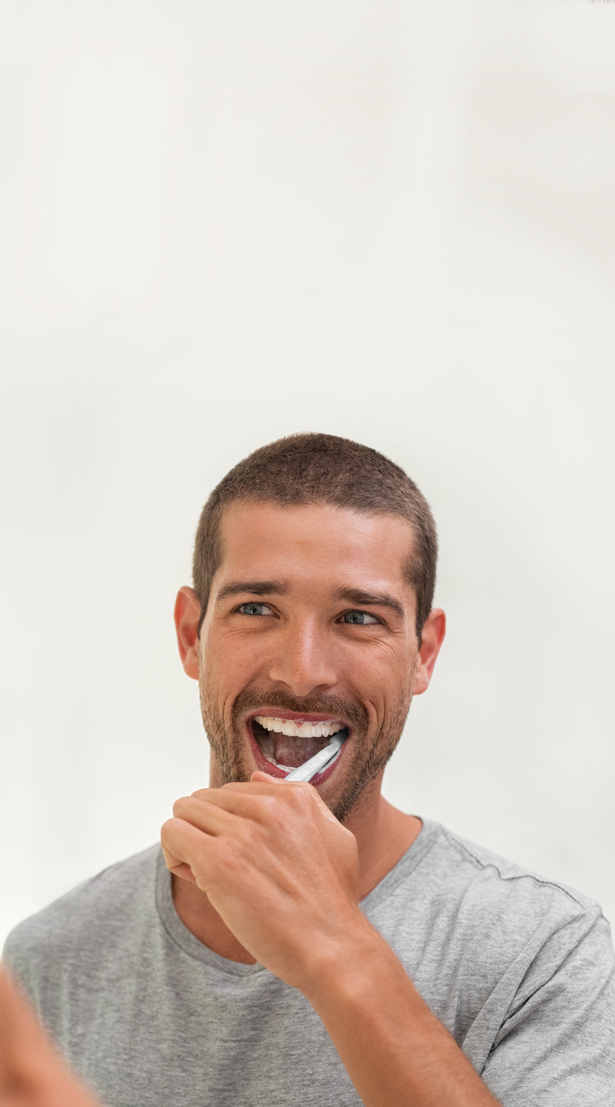Junger Mann mit kurzen braunen Haaren putzt seine Zähne mit einer weißen Hand-Zahnbürste.