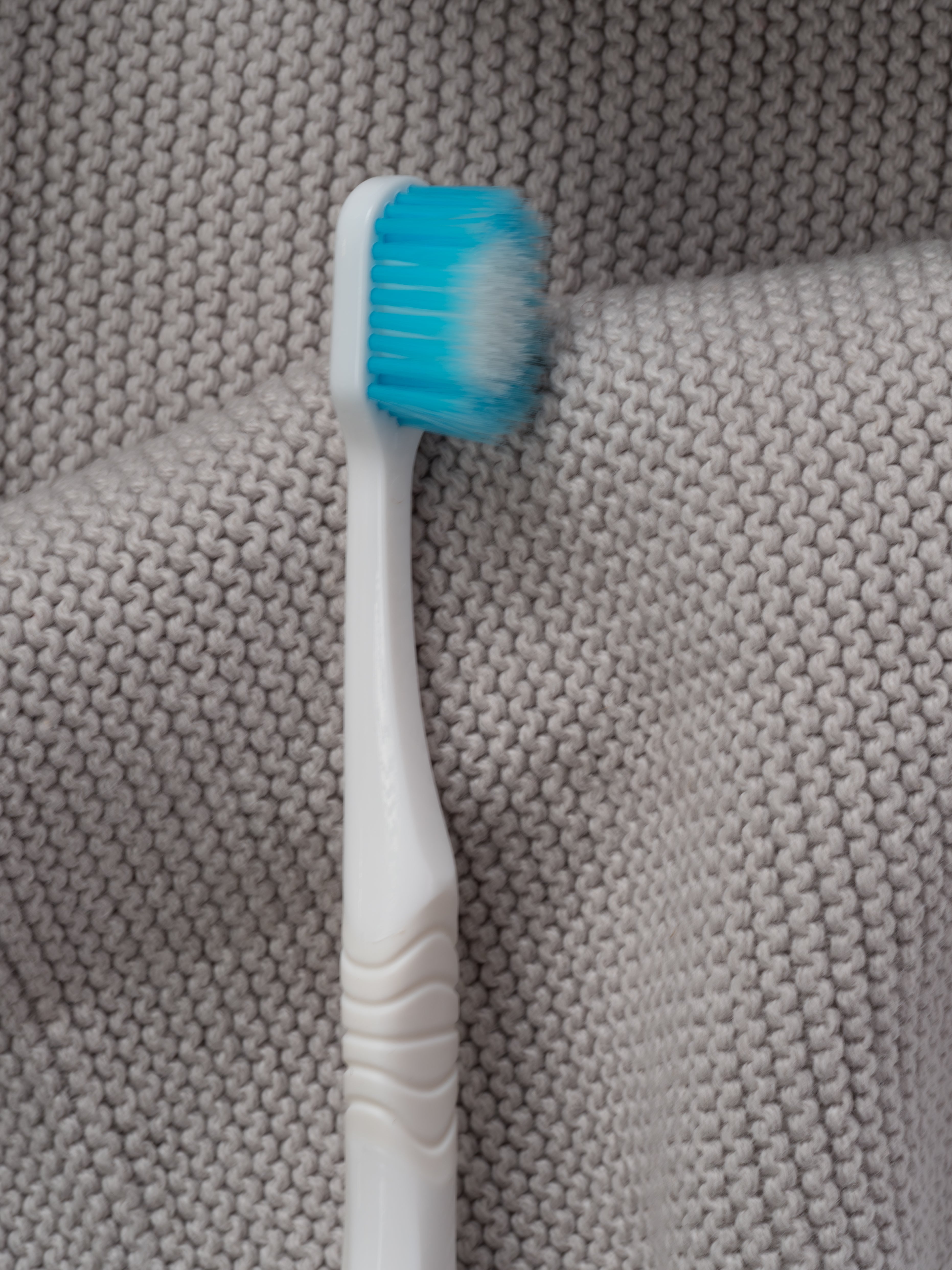 Komfort-Zahnbürste mit sanften hellblauen Borsten auf einem hellgrauen Handtuch liegend.