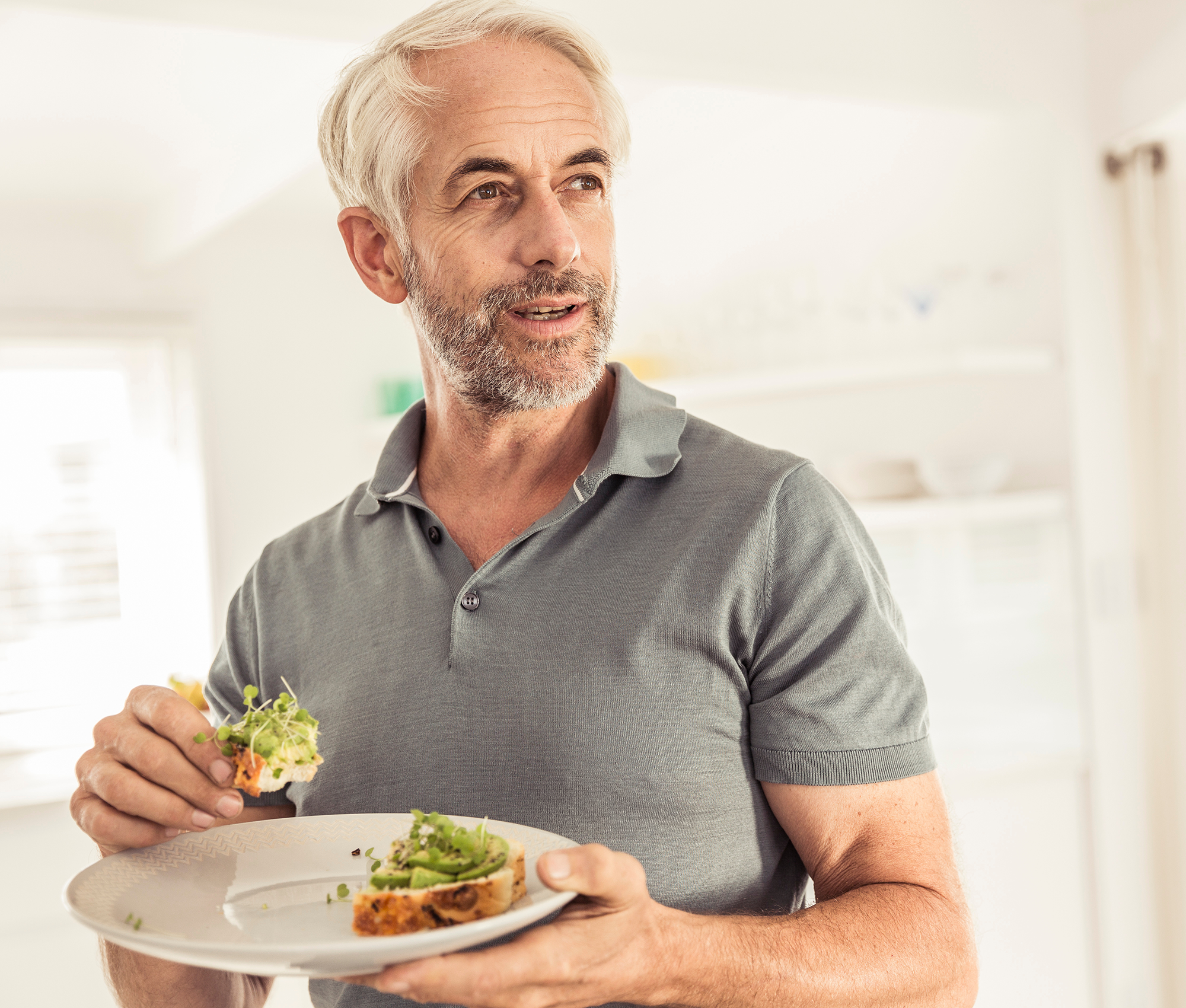 Älterer Herr hält ein Teller mit Brot und Avocado-Aufstrich in den Händen.