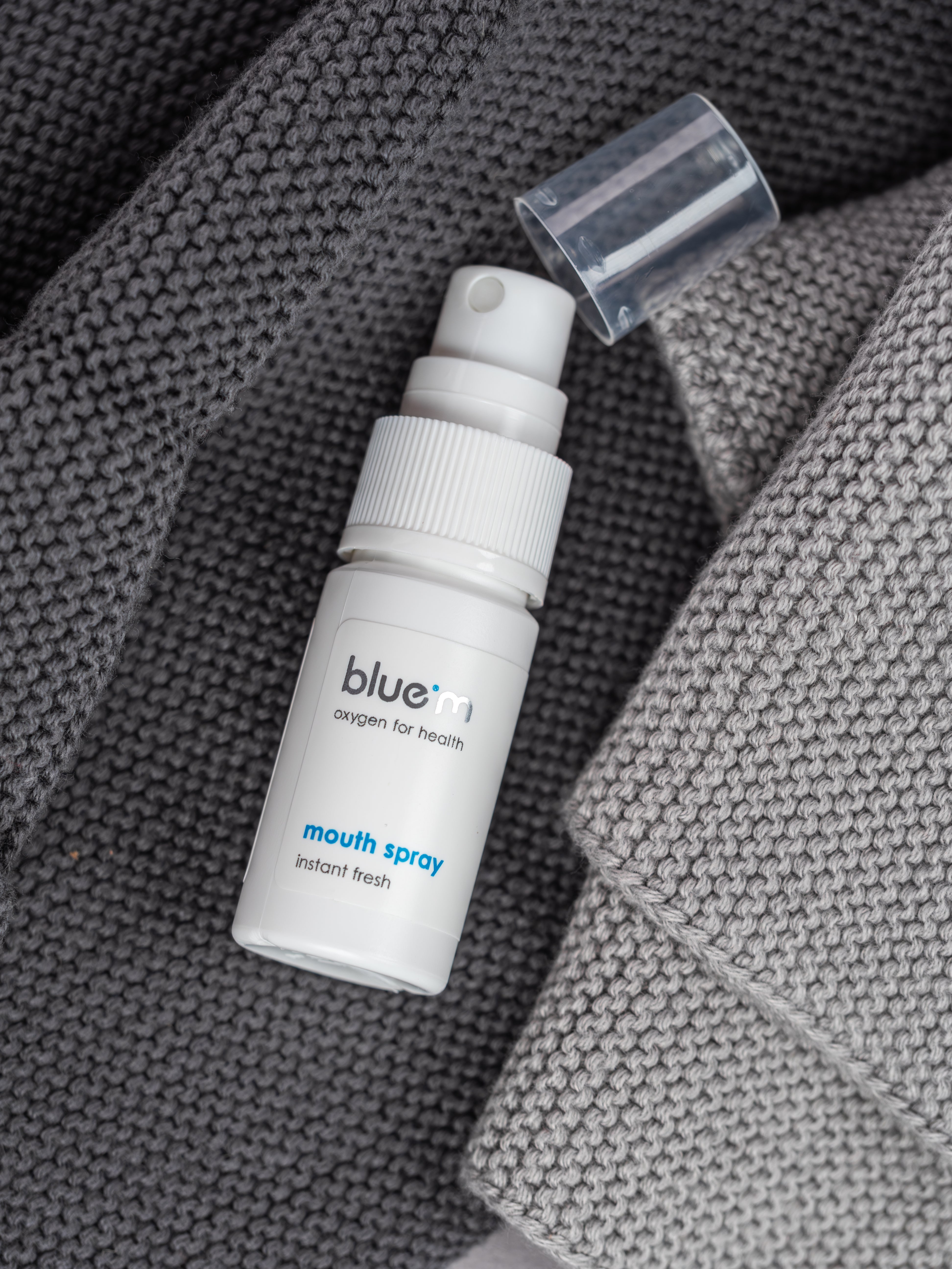 Mundspray liegt geöffneter Abdeckkappe auf einem grauen Handtuch.
