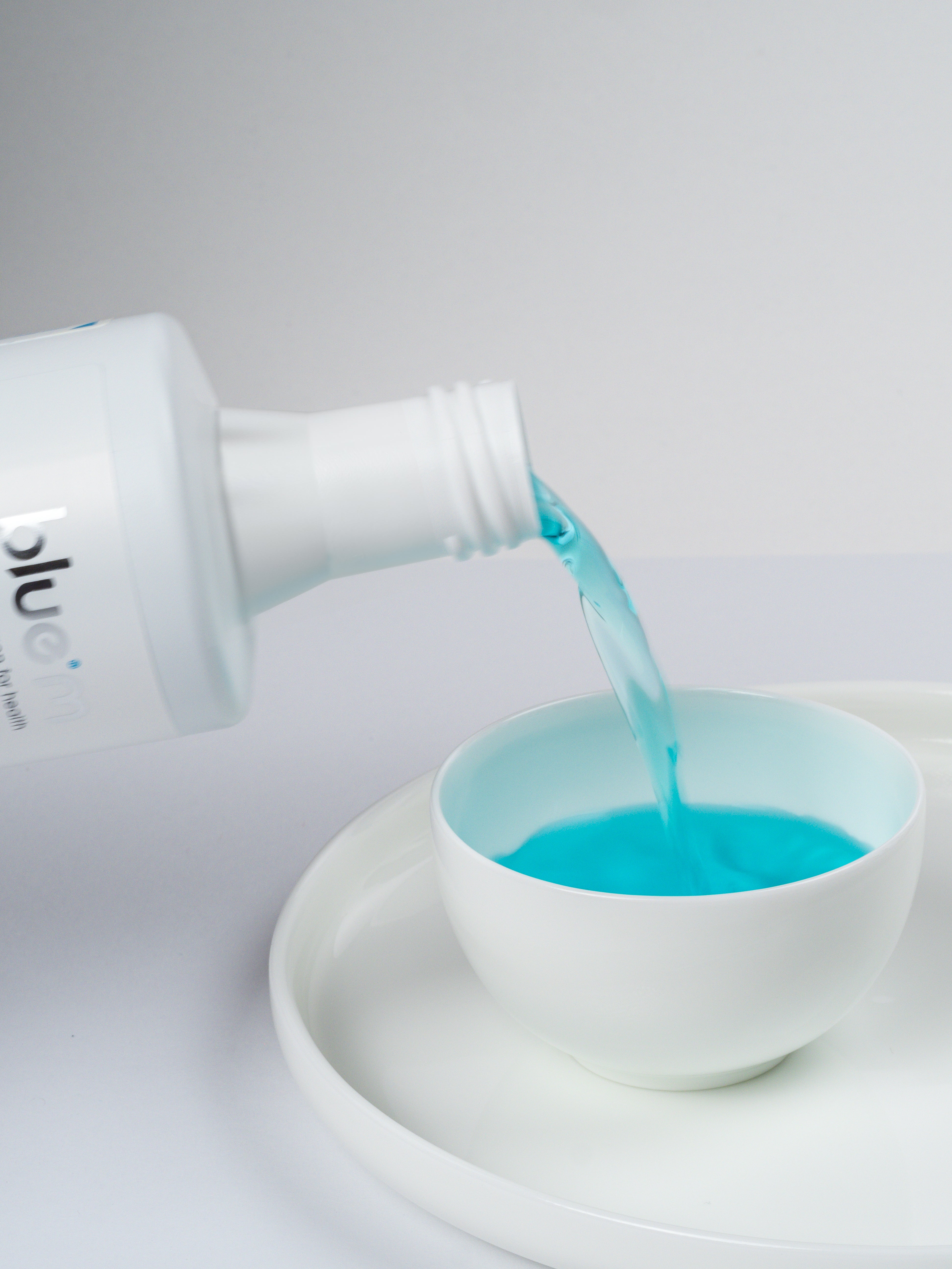 Hellblaue Mundspül-Lösung wird langsam in eine weiße Schale