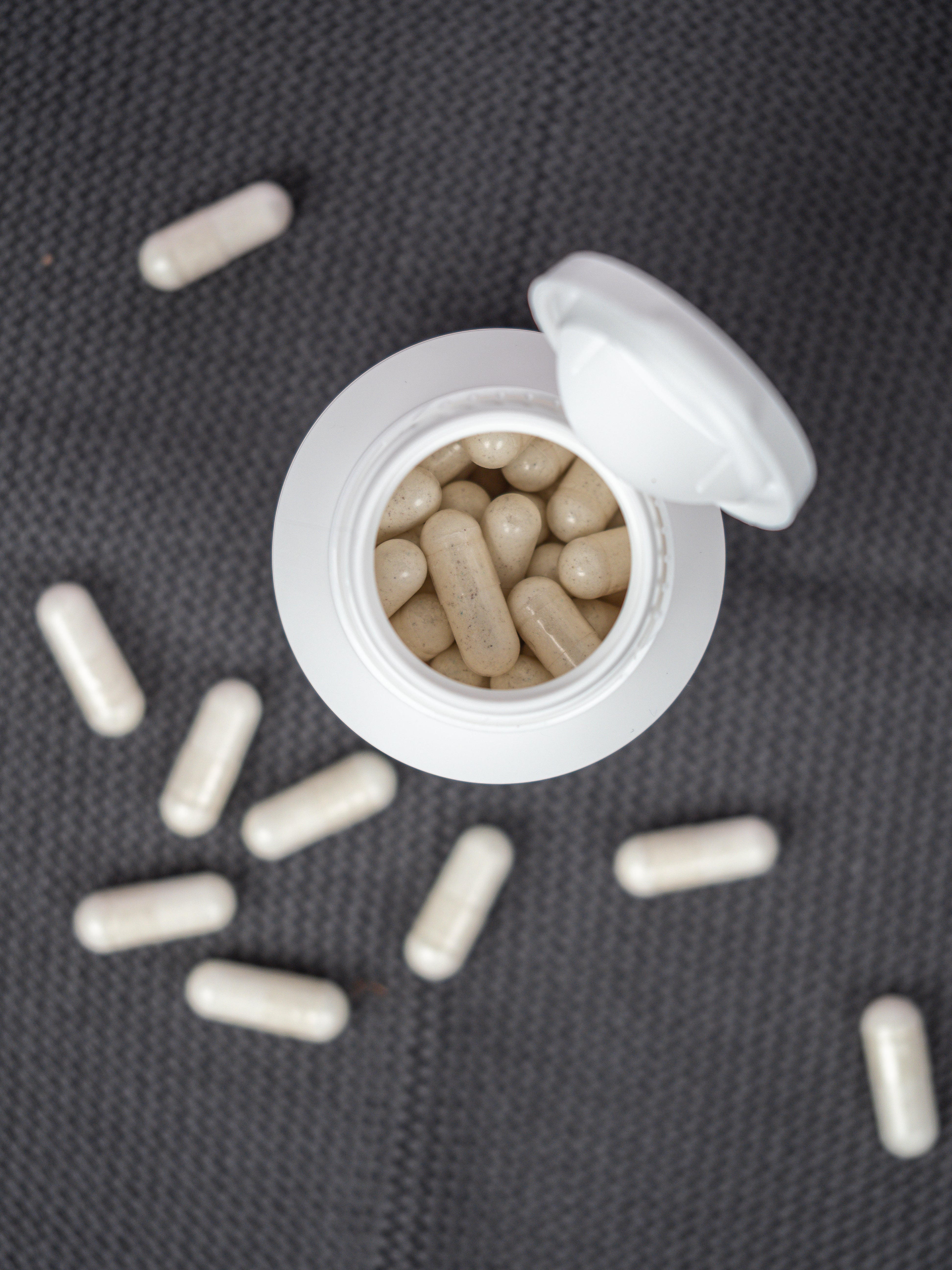Geöffnete Dose von Nahrungsergänzung-Kapseln für Knochen und Zahn, neben der Dose liegen die Kapseln verstreut auf dem Untergrund.