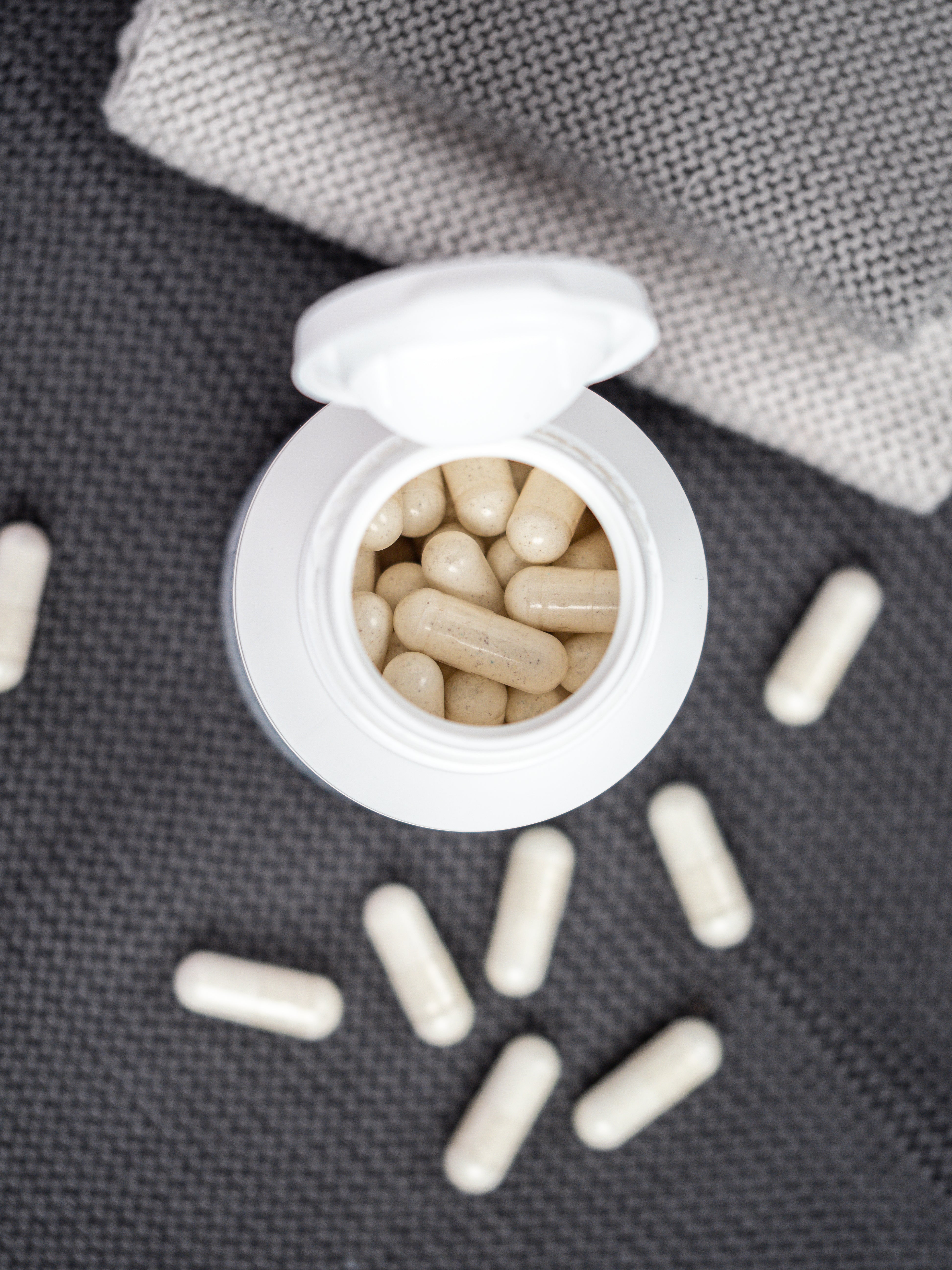 Geöffnete Dose von Nahrungsergänzung-Kapseln für Knochen und Zahn, neben der Dose liegen die Kapseln verstreut auf dem Untergrund.