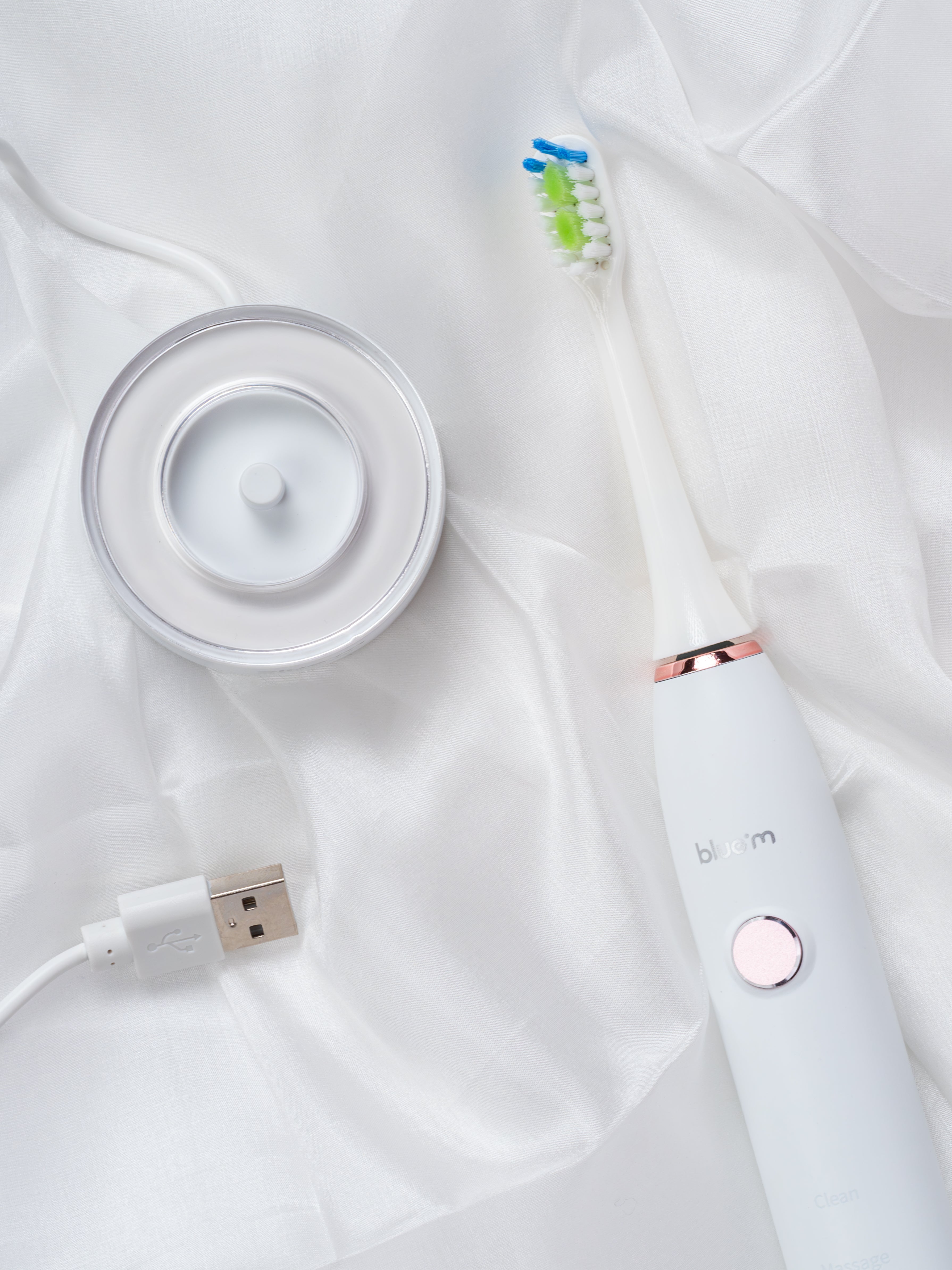 Elektrische Schallzahnbürste mit USB-Ladestation arrangiert auf einem weißen Stofftuch.
