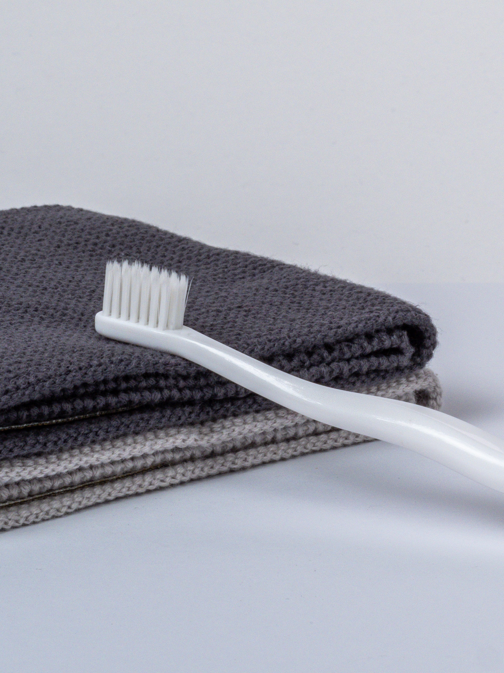 Sensitiv-Zahnbürste mit sanften weißen Borsten auf einem grauen Handtuch liegend.
