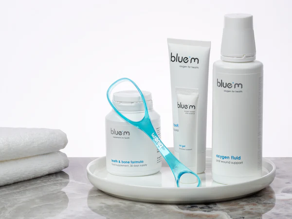 Pflegeset zur Implantatpflege bestehend aus Nahrungsmittelergänzung in Form von Kapseln, Zungenreiniger, Zahngel, Wundgel und Sauerstoff-Fluid. Die Produkte sind auf einem weißen Tablett arrangiert.