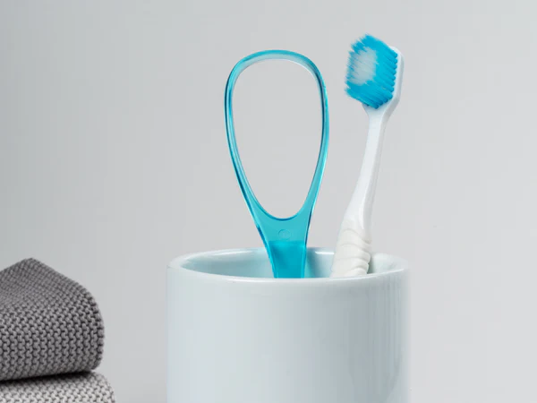 Zungenreiniger und Zahnbürste stehen in einem Zahnputzbecher