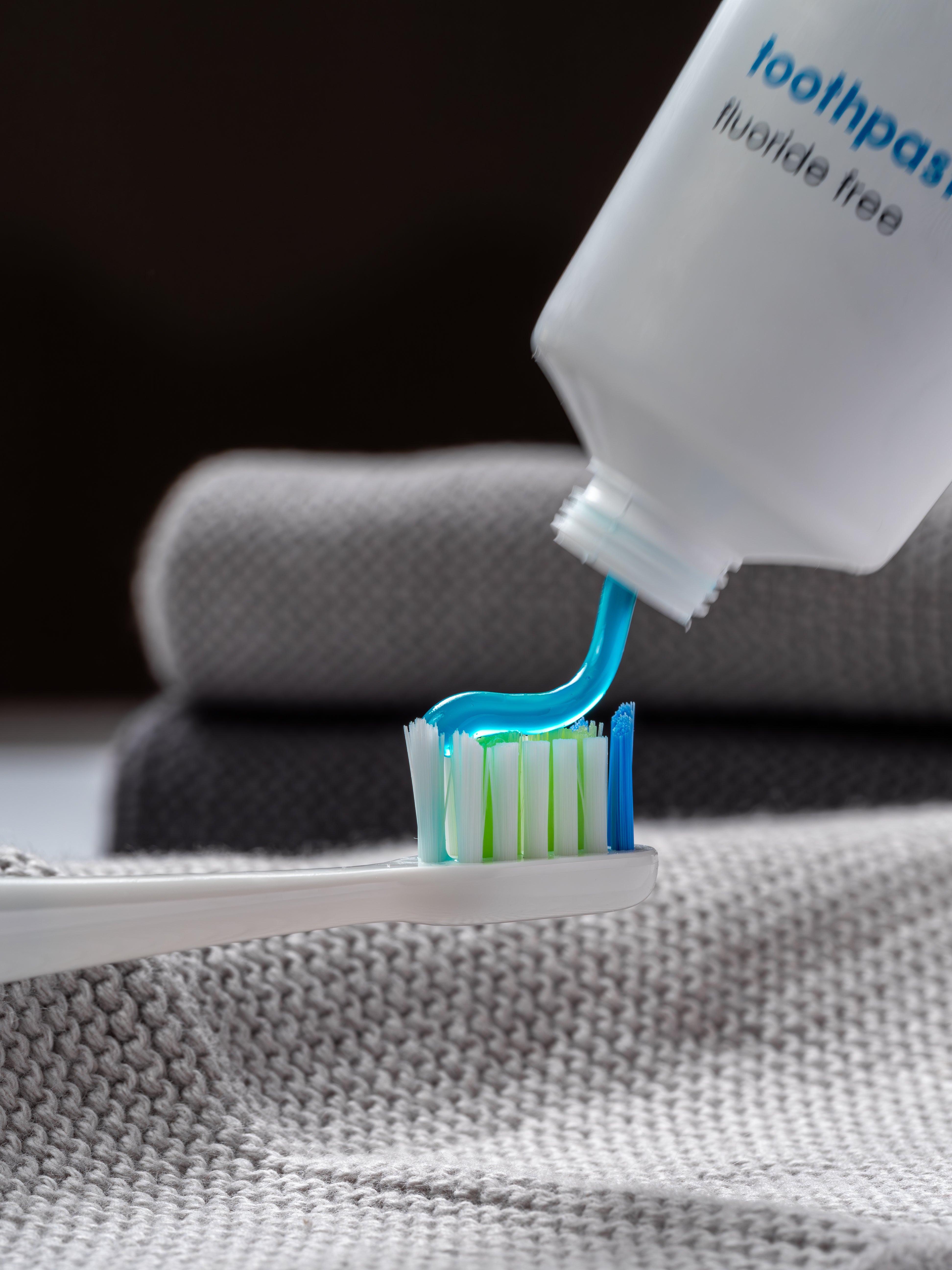 Eine senkrecht gehaltene Tube Zahngel ohne Fluorid aus der das hellblaue Gel auf eine Zahnbürste fließt.