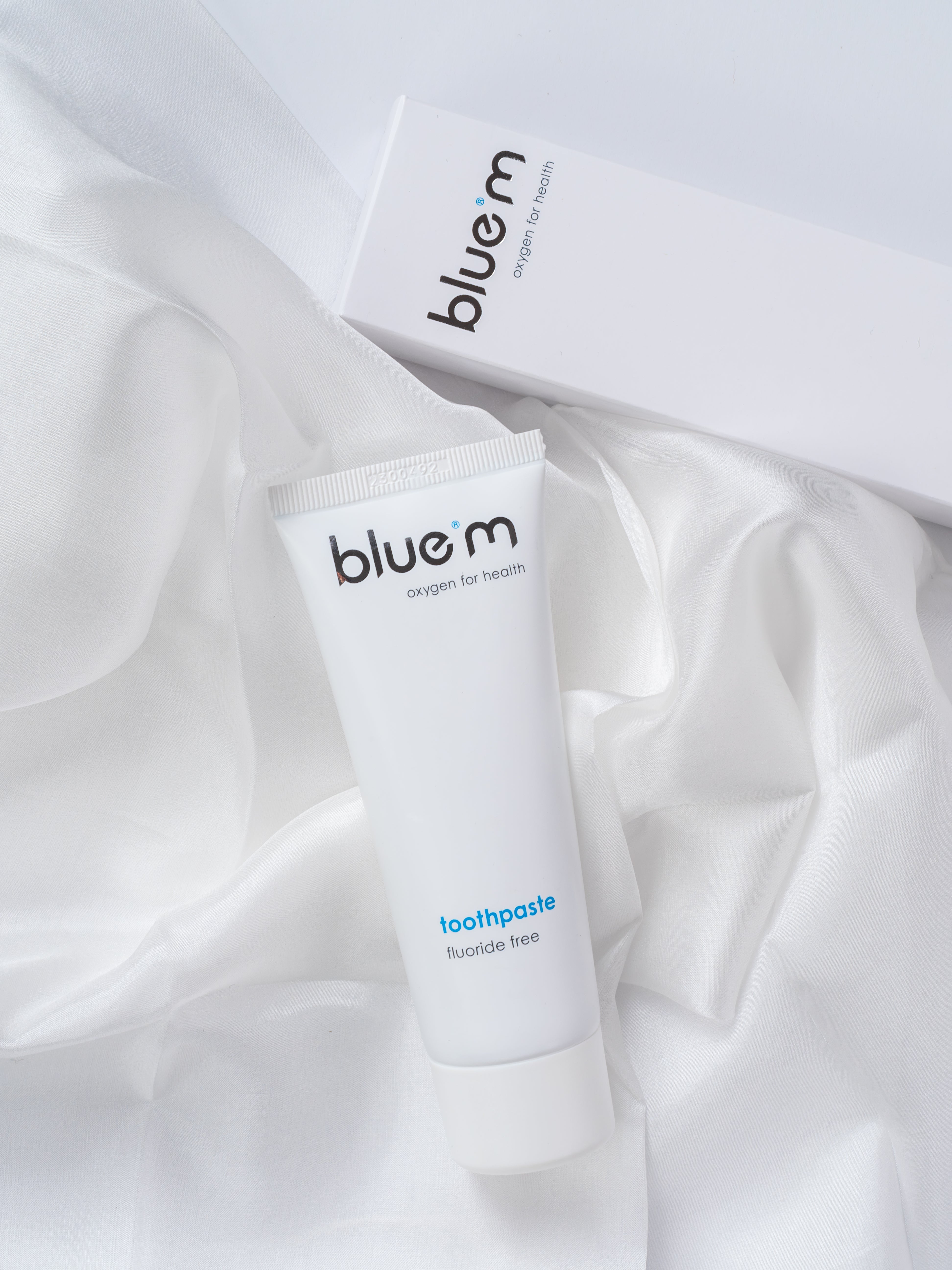 Eine Tube Zahngel ohne Fluorid auf einem weißen Stofftuch arrangiert, dahinter ist die Umverpackung erkennbar.