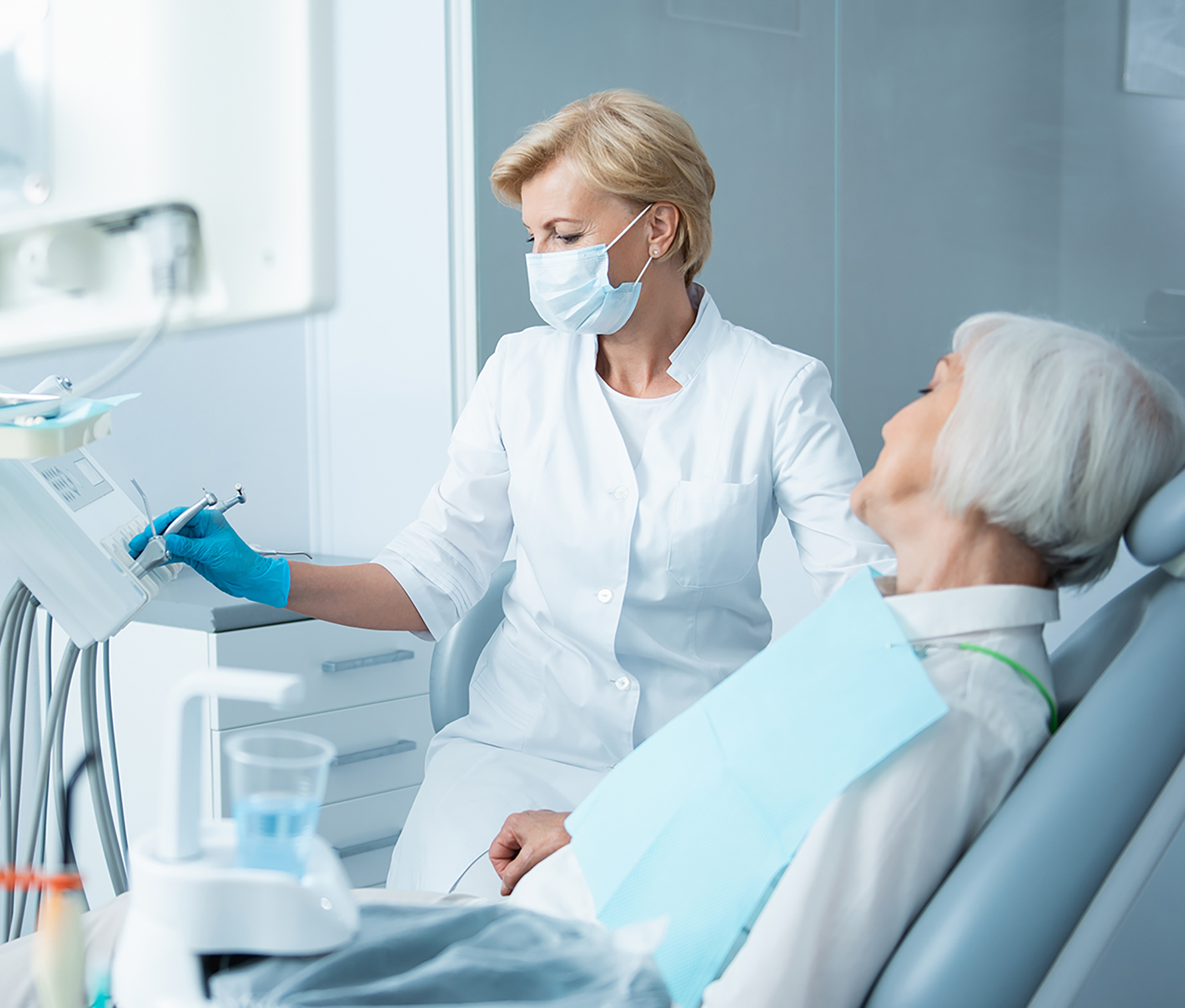 Zahnärztin und ältere Patientin sind gemeinsam im Behandlungszimmer einer Zahnarztpraxis. Die Zahnärztin greift nach den Behandlungsinstrumenten, die Patienten ist der Zahnärztin zugewandt.