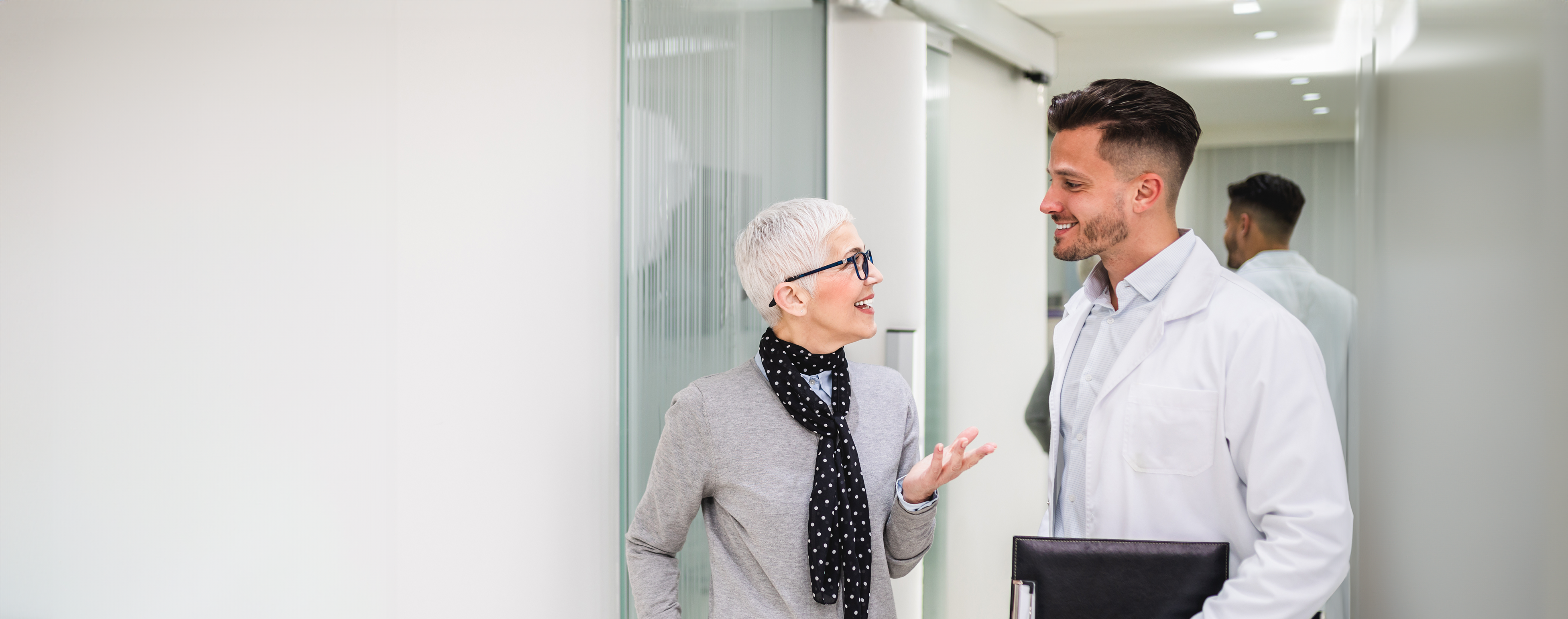 Zahnarzt und ältere Patientin mit kurzen weißen Haaren befinden sich in einer Beratungssituation in einer Zahnarztpraxis.