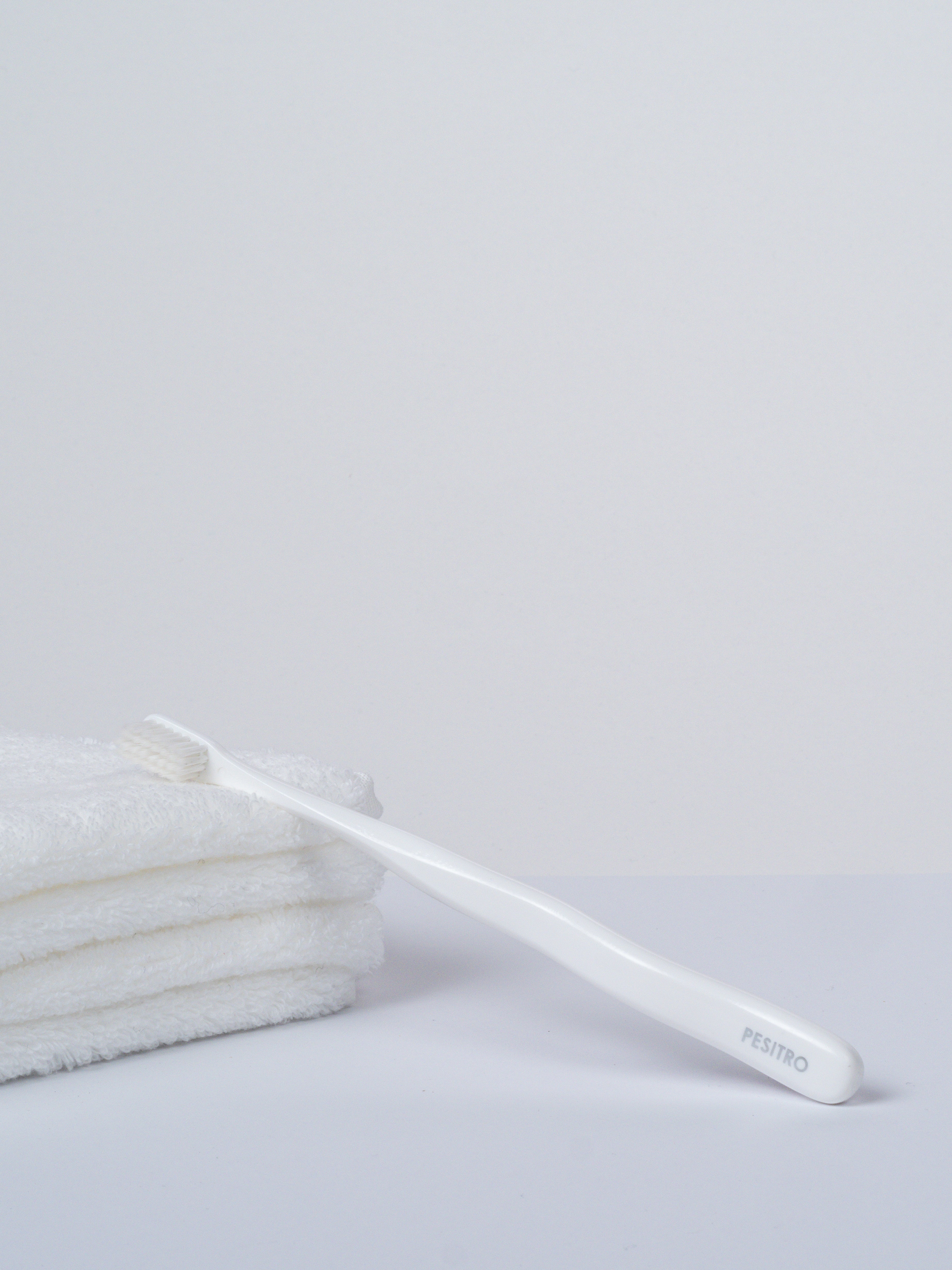 Sensitiv-Zahnbürste mit sanften weißen Borsten seitlich auf einem weißen Handtuch liegend.