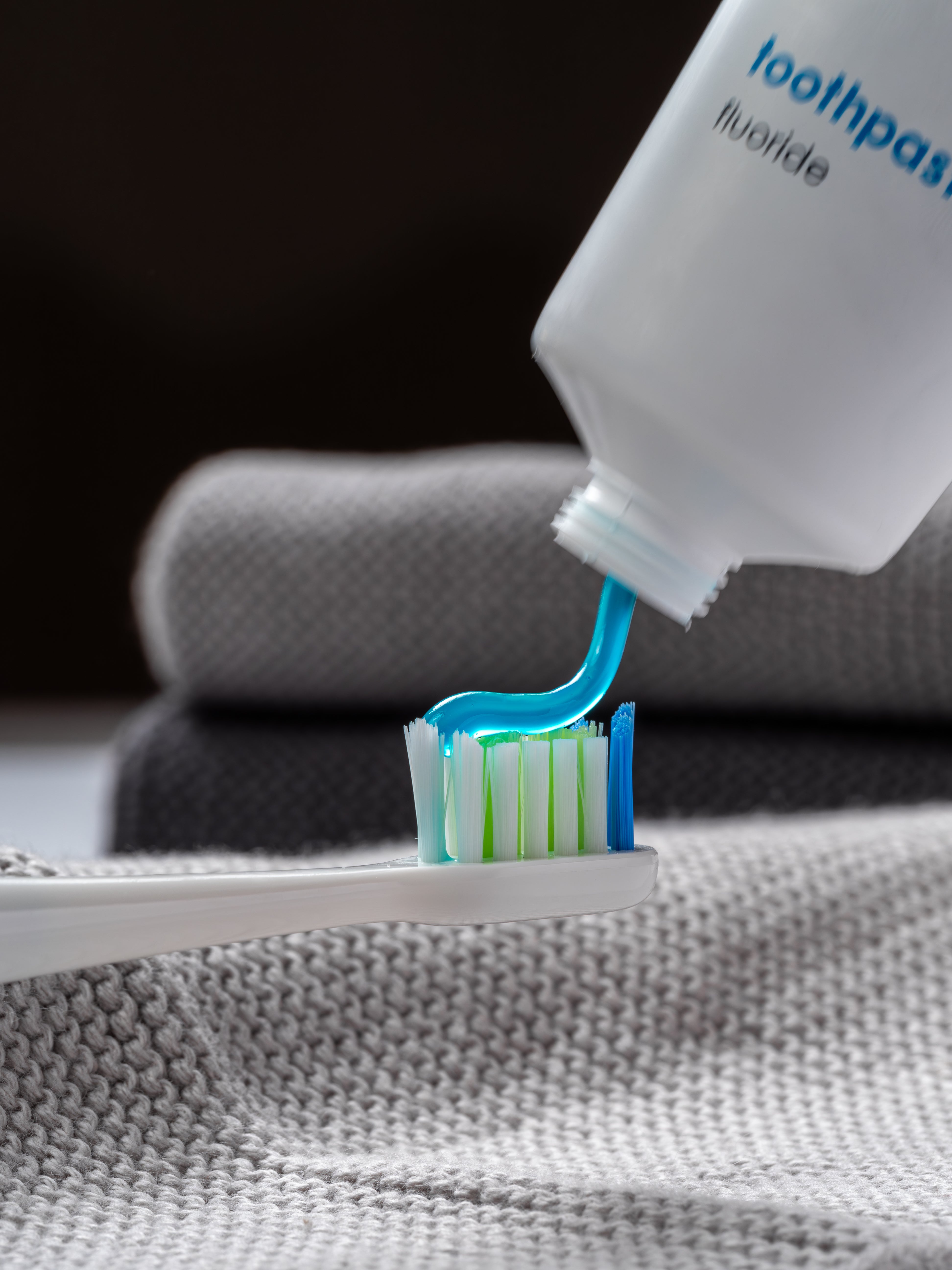Eine senkrecht gehaltene Tube Zahngel mit Fluorid aus der das hellblaue Gel auf eine Zahnbürste fließt.