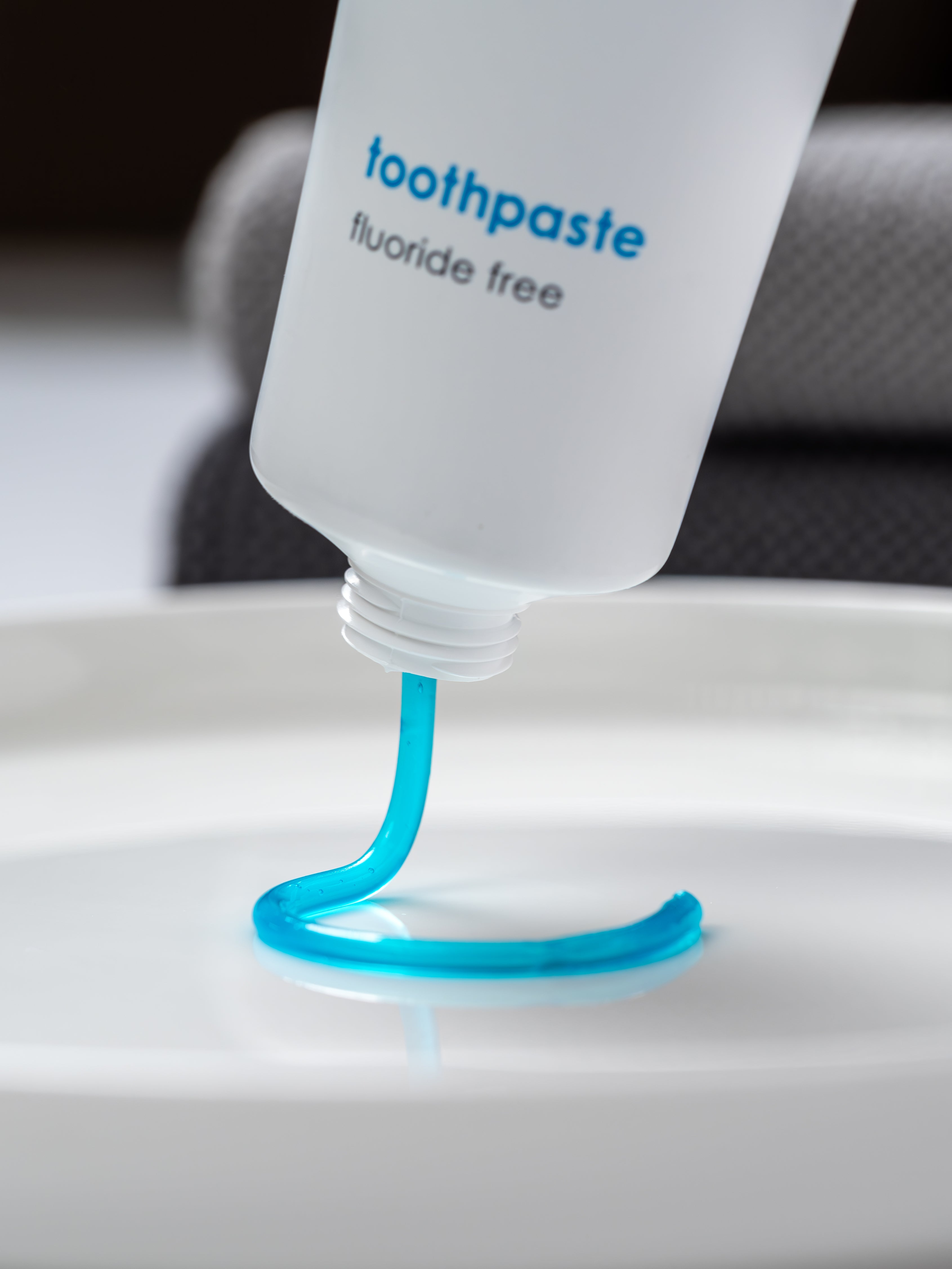 Eine senkrecht gehaltene Tube mit Zahngel ohne Fluorid aus der das hellblaue Gel kreisförmig herausfließt.