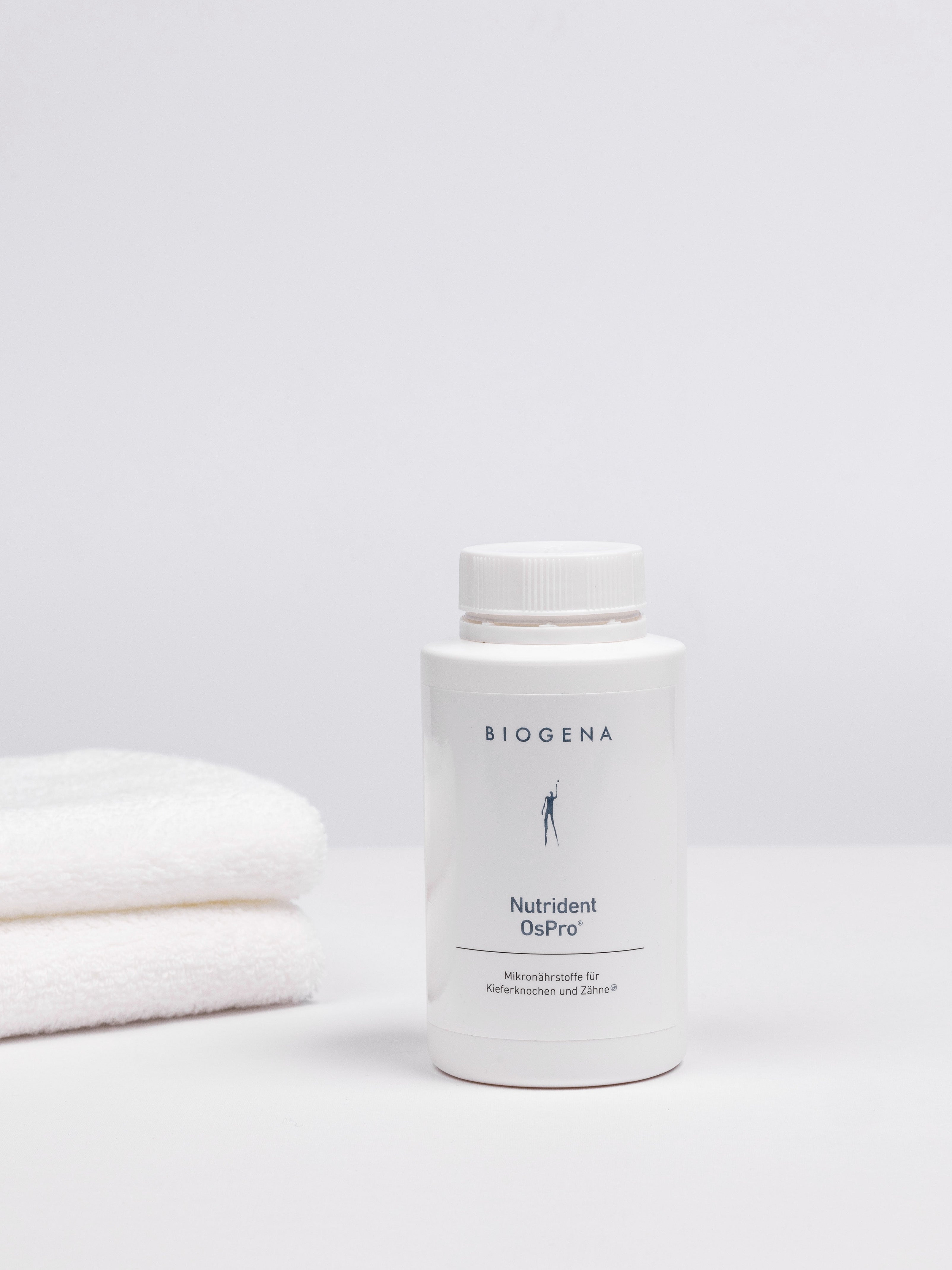 Geschlossene Verpackungsdose Biogena Nutrident OsPro, links daneben ein Stapel weißer Handtücher.
