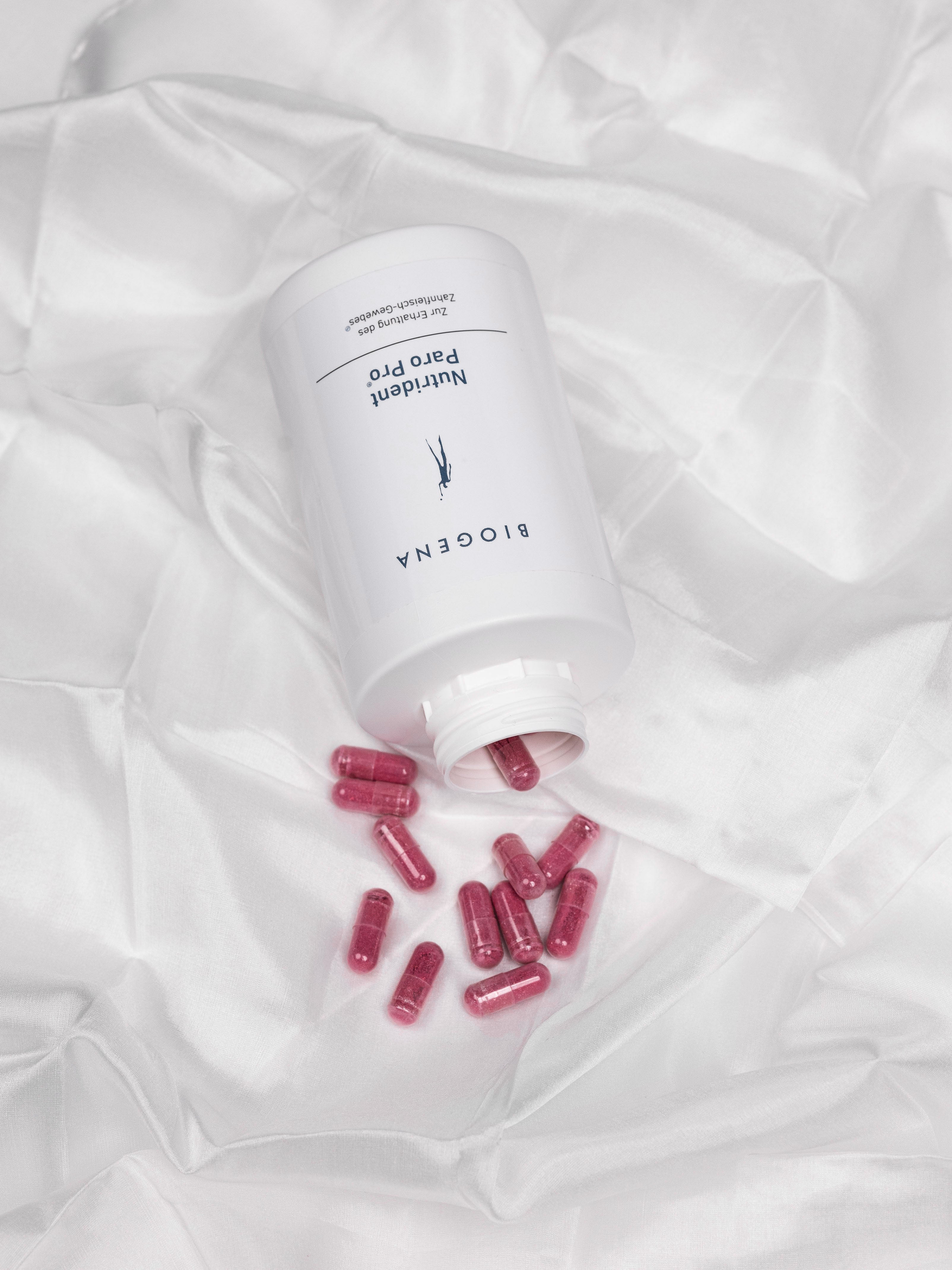 Verpackungsdose von Nutrident Paro Pro liegend auf einem weißen Tuch, die enthaltenen roten Kapseln liegen vor der Verpackung.