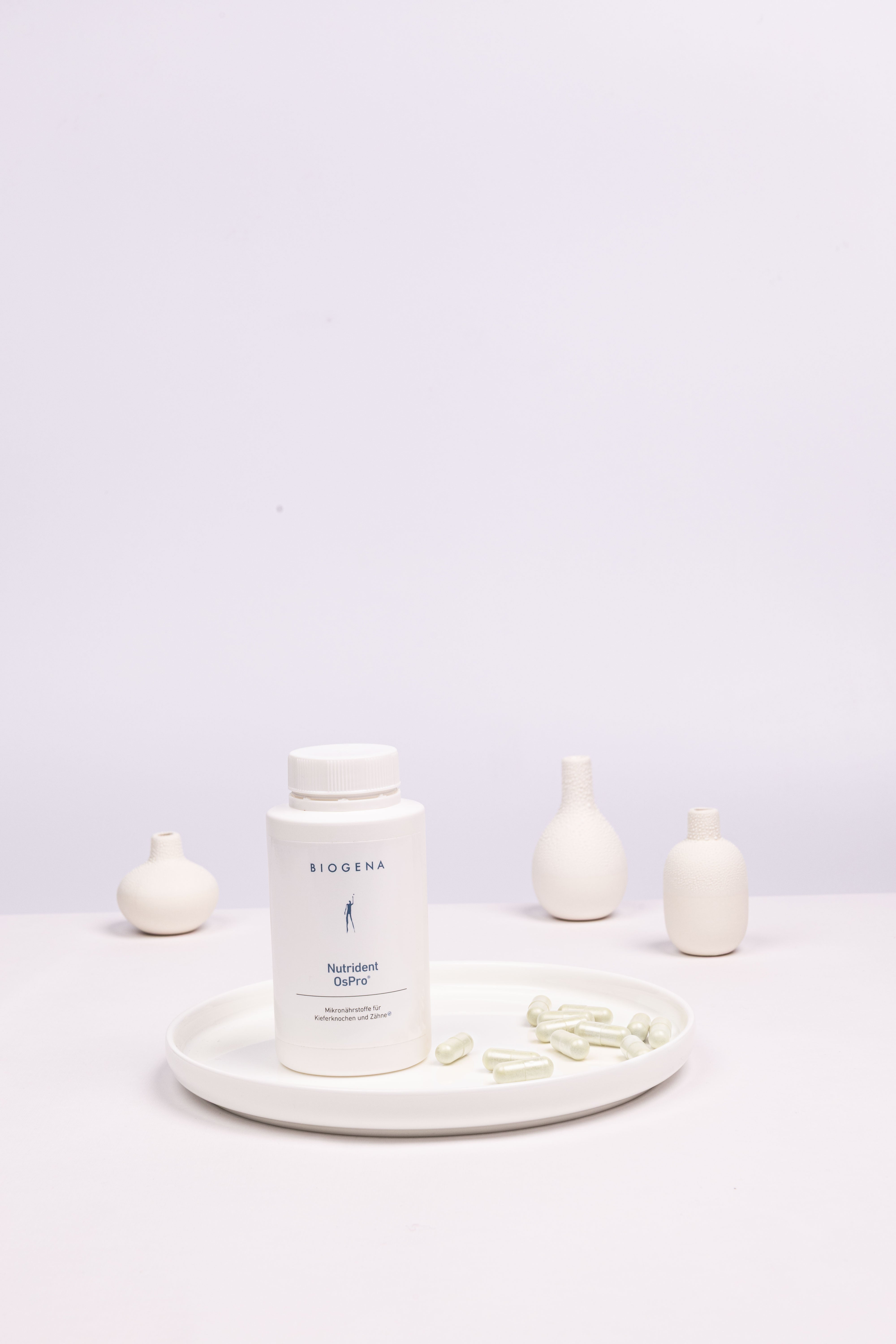 Geschlossene Verpackung von Biogena Nutrident OsPro steht auf einem weißen Tablett umgeben von weißen Kapseln.