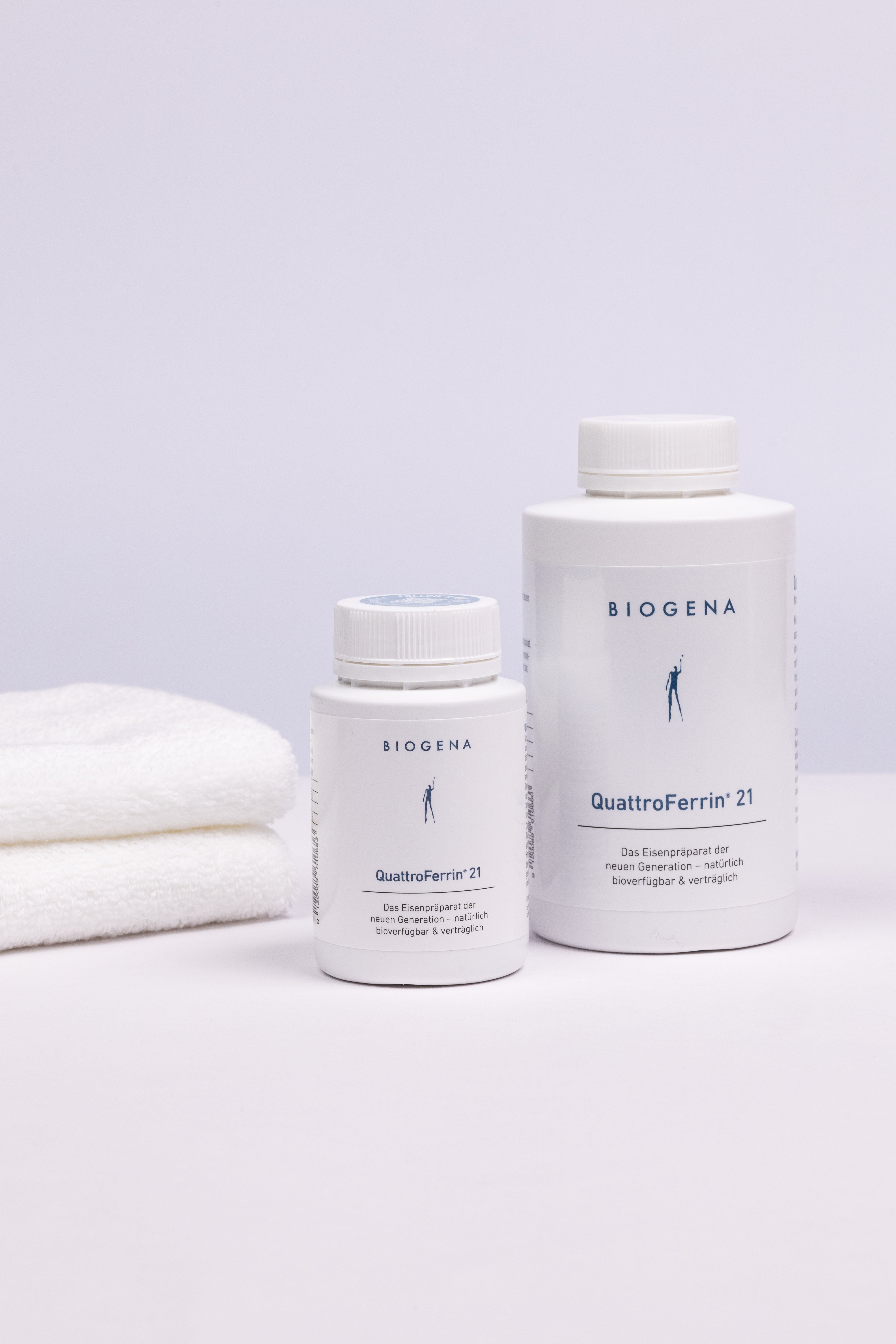 Zwei Dosen QuattroFerrin 21 unterschiedlicher Verpackungsgrößen stehend, links daneben ein Stapel weißer Handtücher.