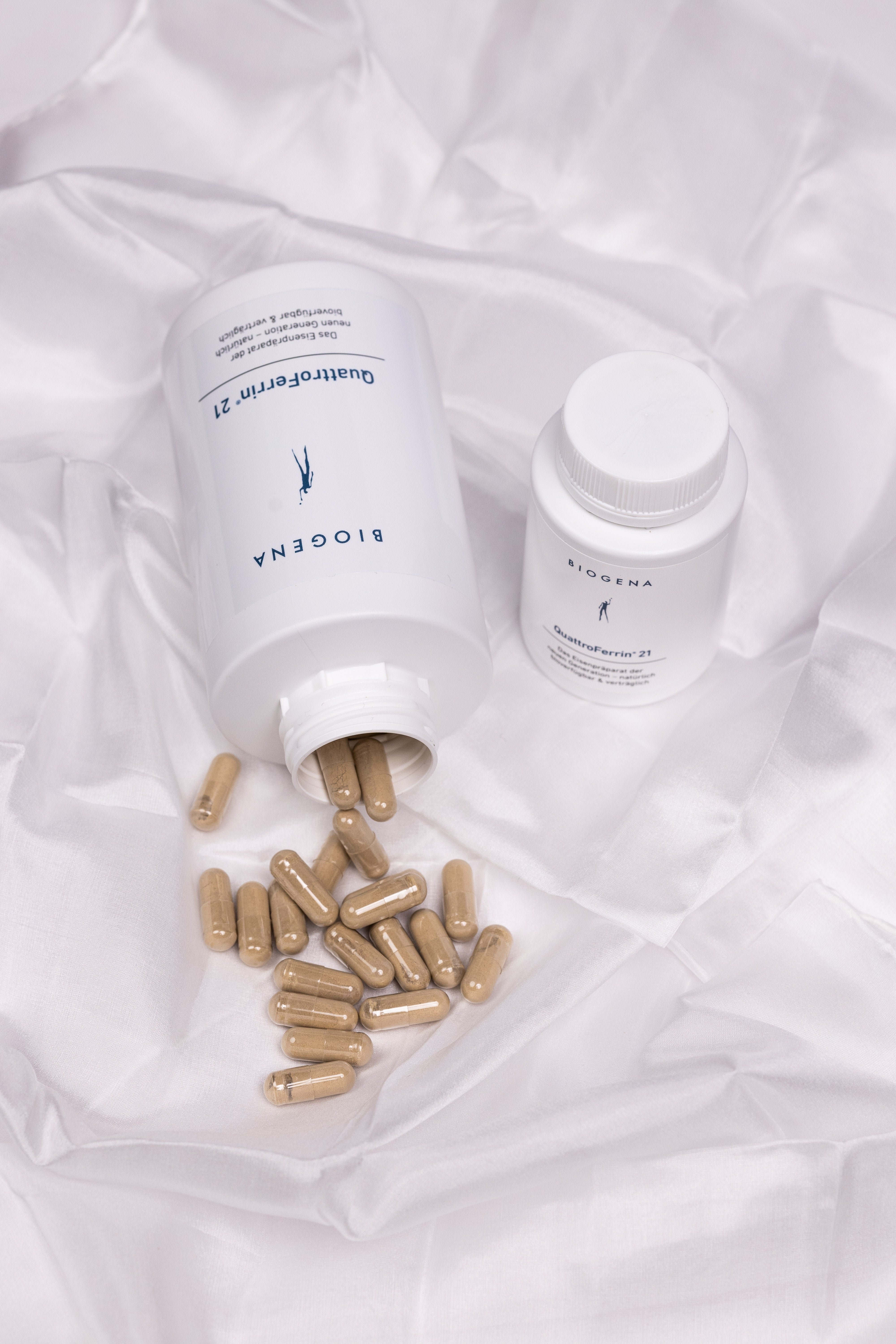 Verpackungsdose von QuattroFerrin® 21 liegend auf einem weißen Tuch, die enthaltenen Kapseln liegen vor der Verpackung.