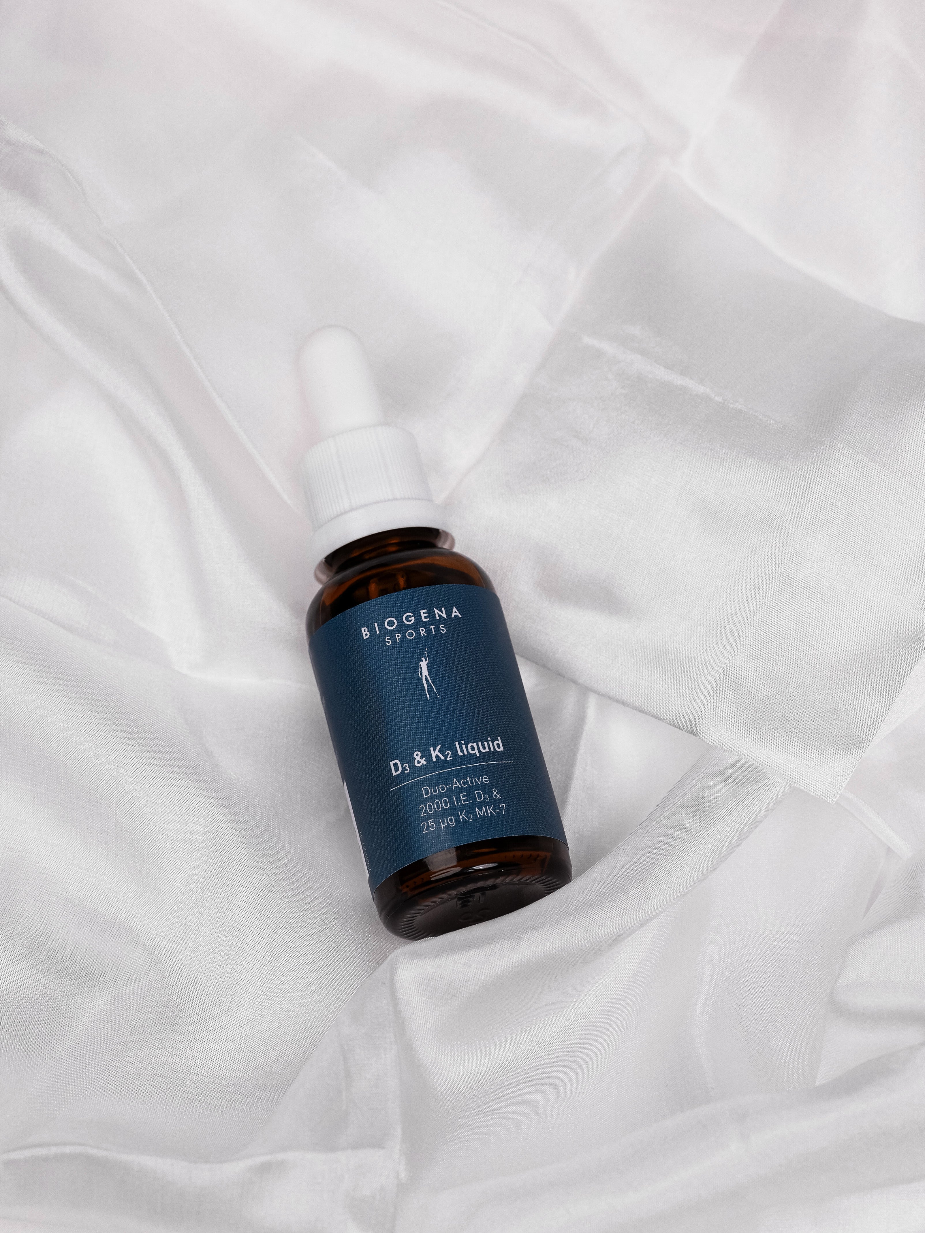 BIOGENA SPORTS D3 & K2 liquid Flasche auf einem weißen Stofftuch liegend.