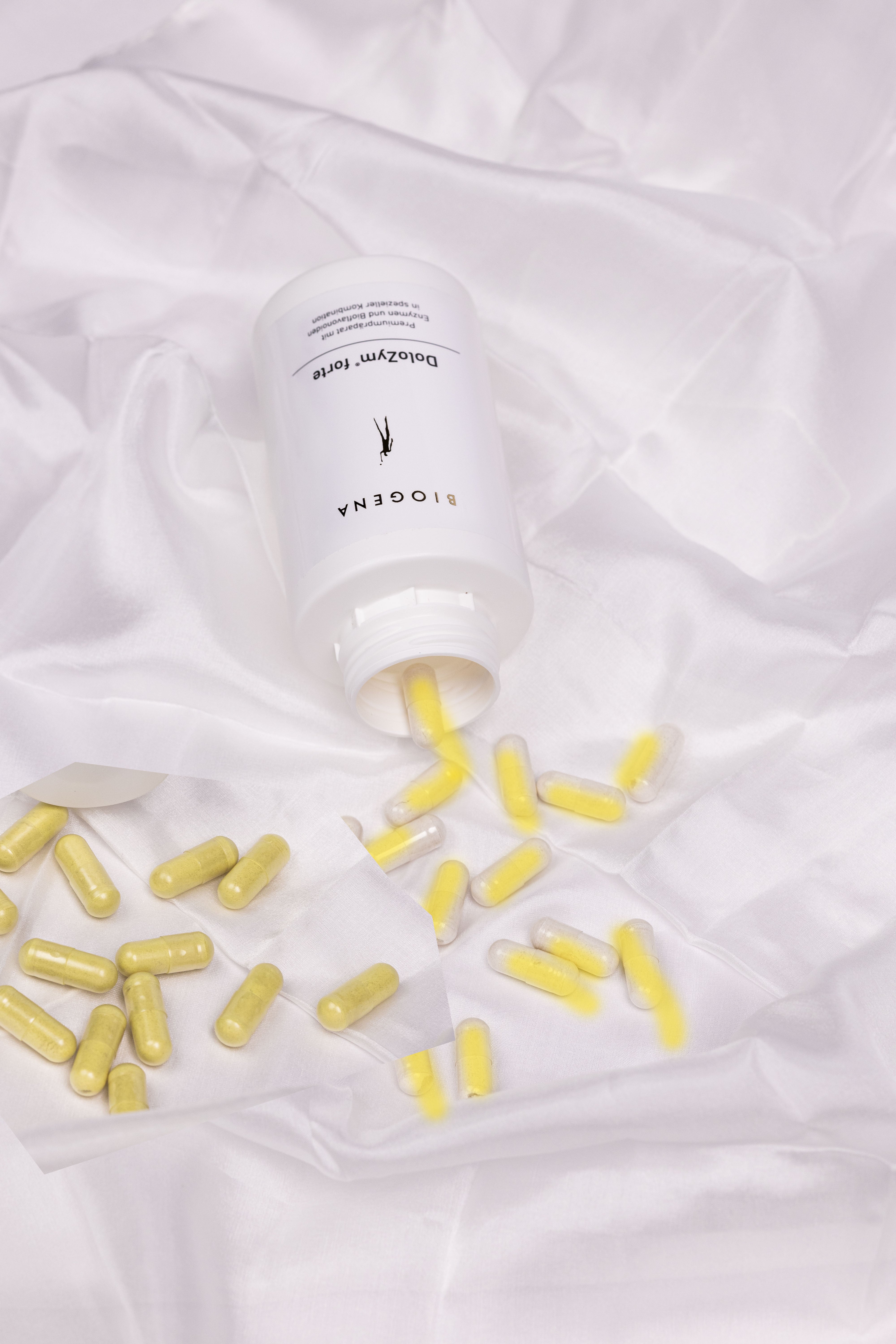 Verpackungsdose liegend auf einem weißen Tuch, gelbe Kapseln liegen vor der Verpackung