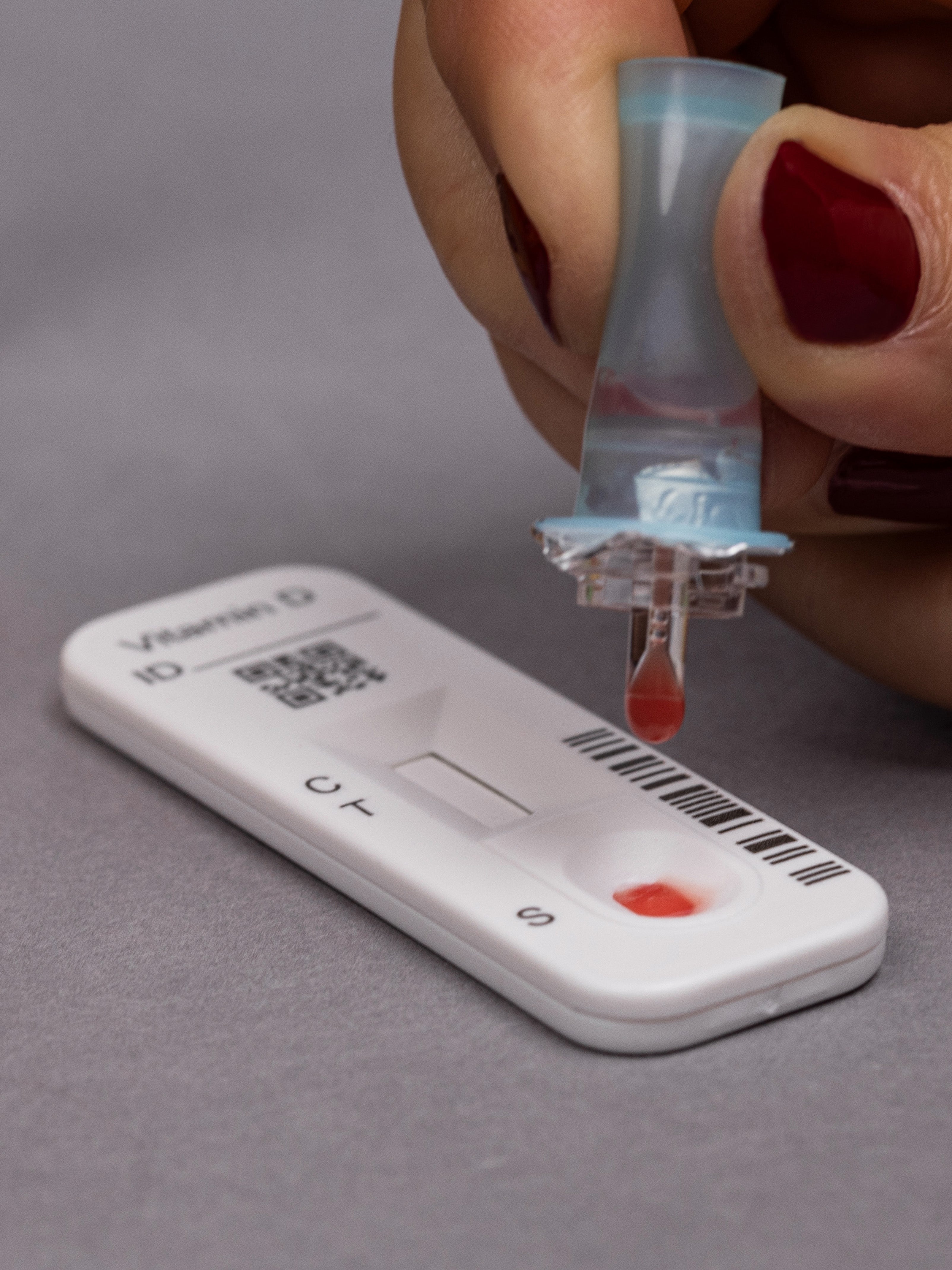 Testvorgang des Vitamin-D Gehalts, dabei hält eine Frauenhand das Probendöschen mit Pufferlösung und Blut in den Händen und tropft einen Tropfen der Lösung auf die Testkassette.